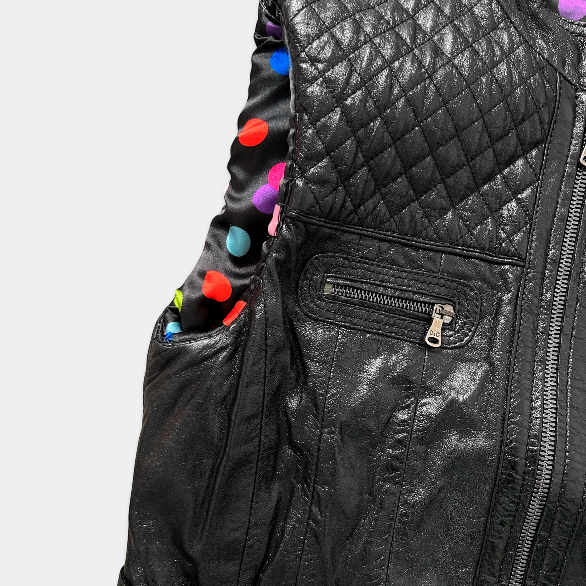 A close-up view of a black leather jacket with a quilted pattern and colorful polka dots on the inside lining.