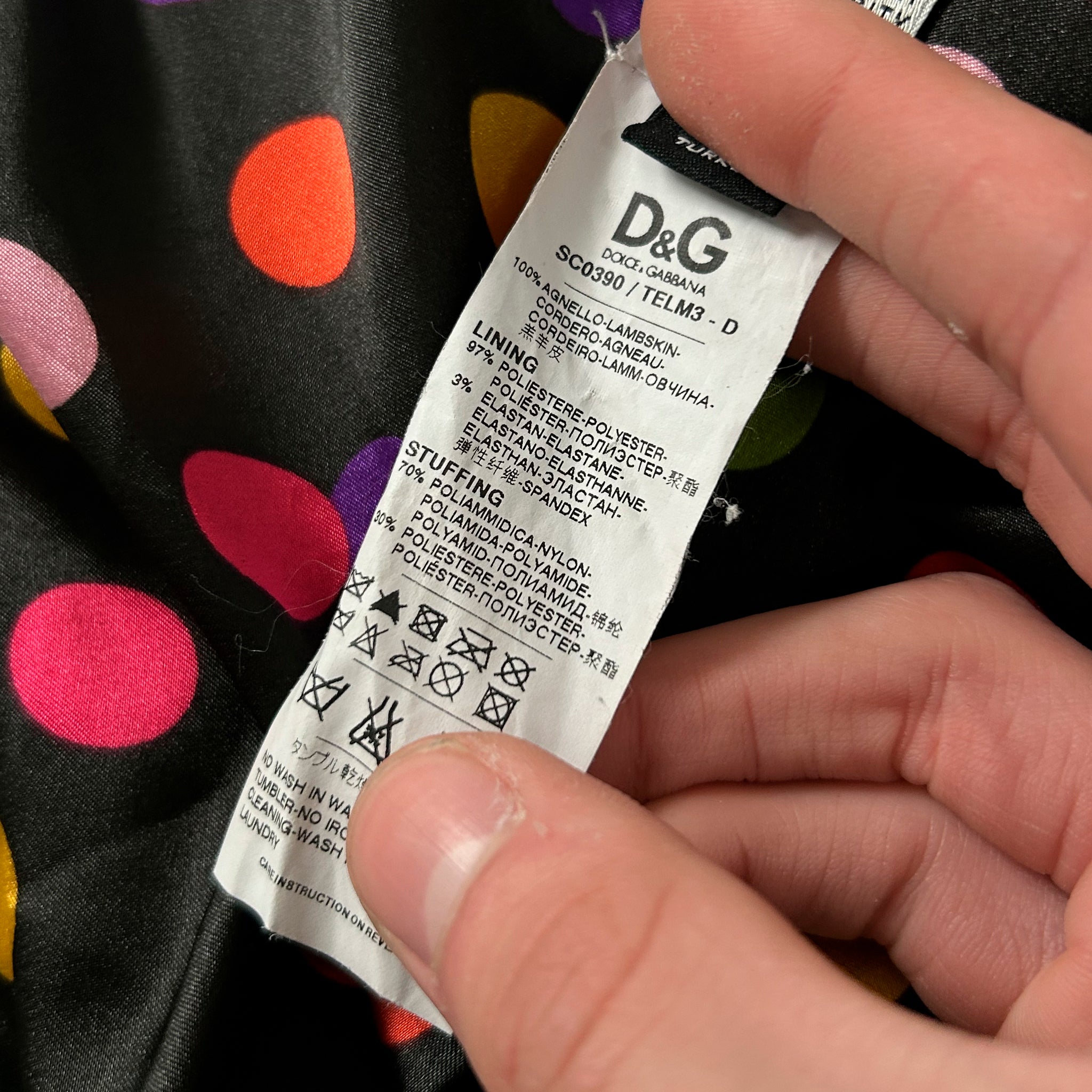 A person's hand holding a label with text and symbols, against a background with a polka dot pattern.