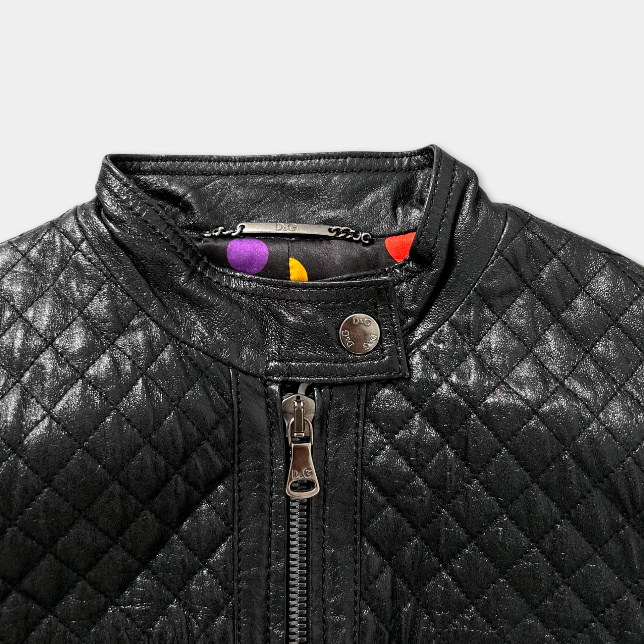 A close-up view of a black quilted leather jacket with a zipper and a small metal tag attached to the collar.