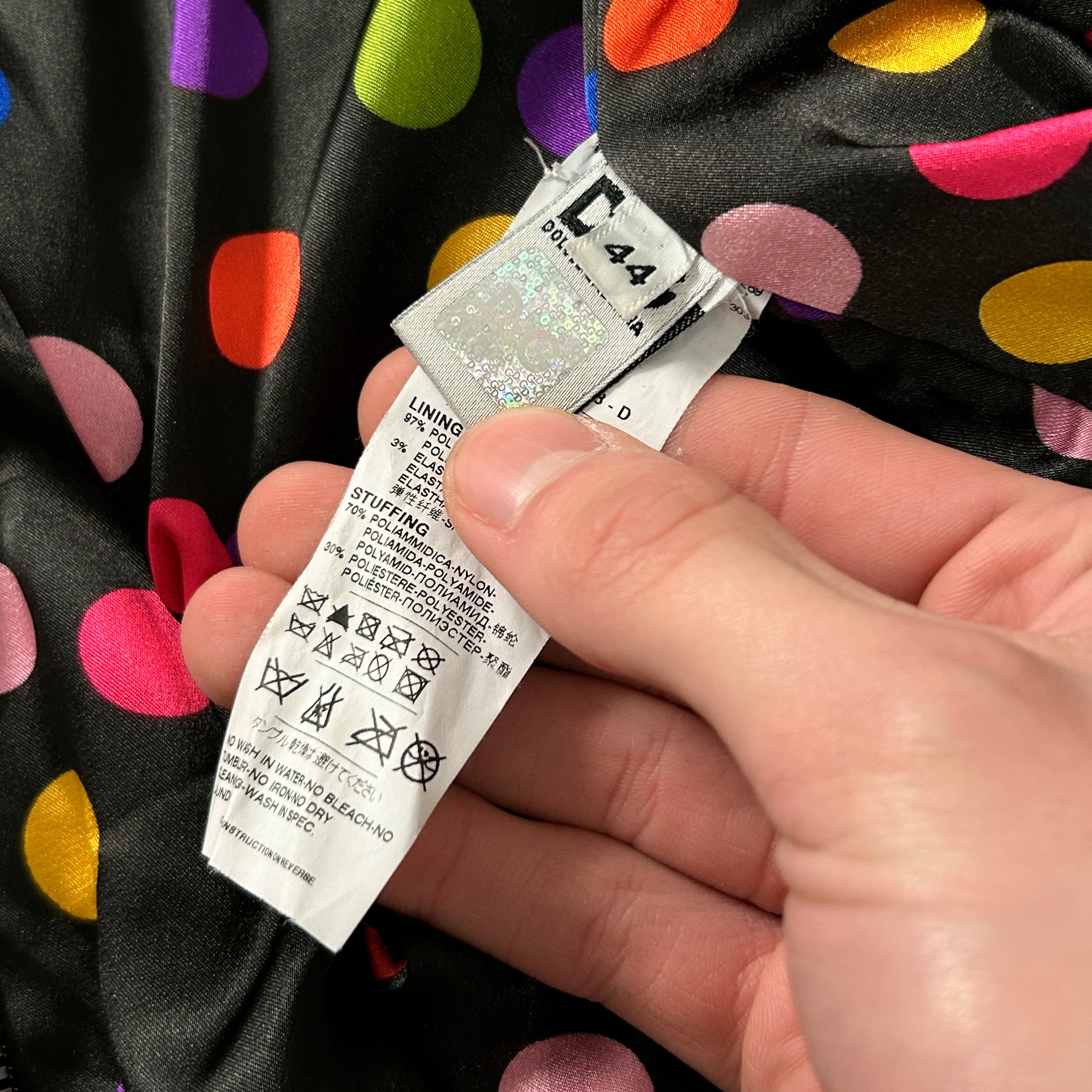 A hand holding a colorful polka dot fabric with a label attached to it.