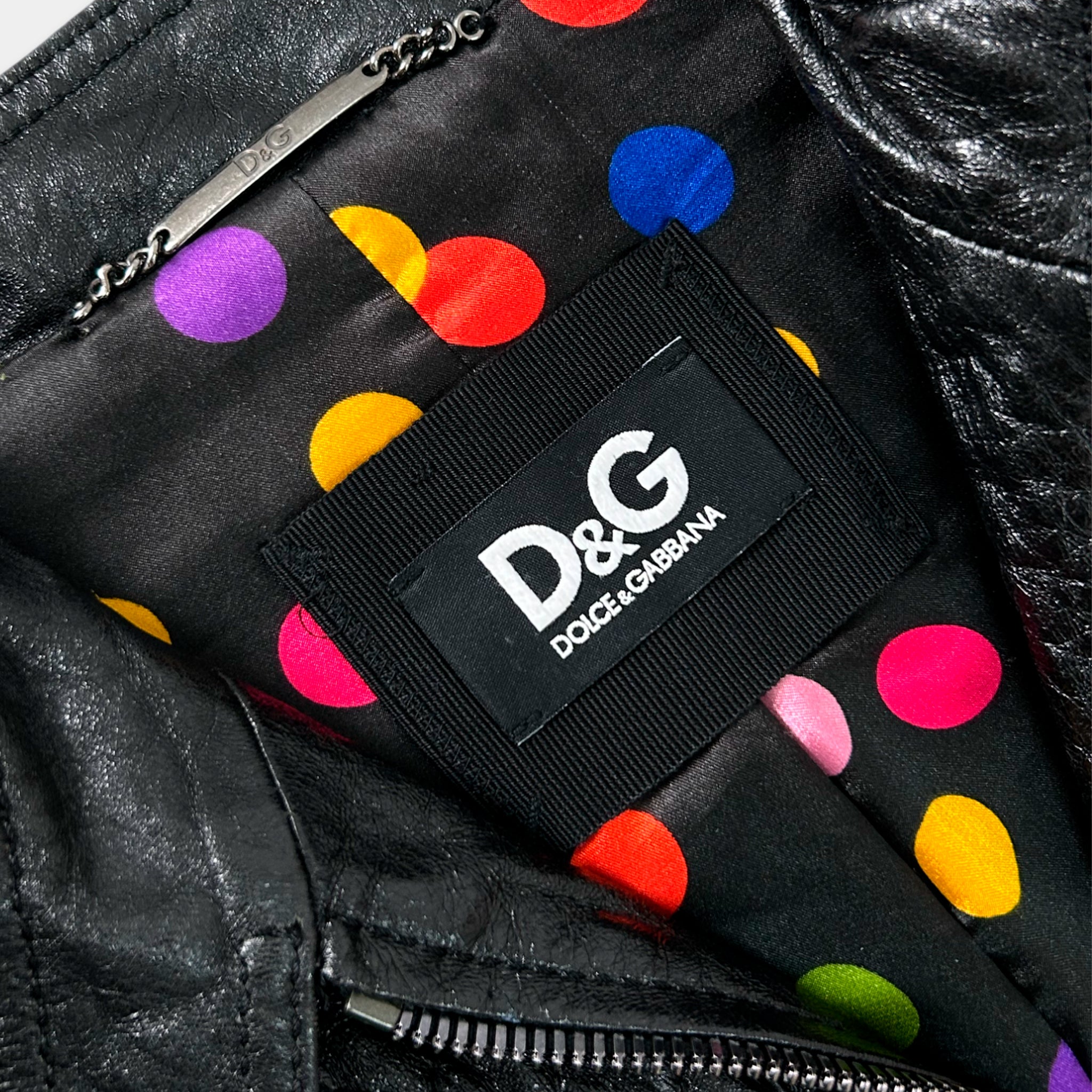 a close-up view of a black leather jacket with a colorful polka dot pattern. The jacket has a label on it that reads "D&G Dolce & Gabbana".