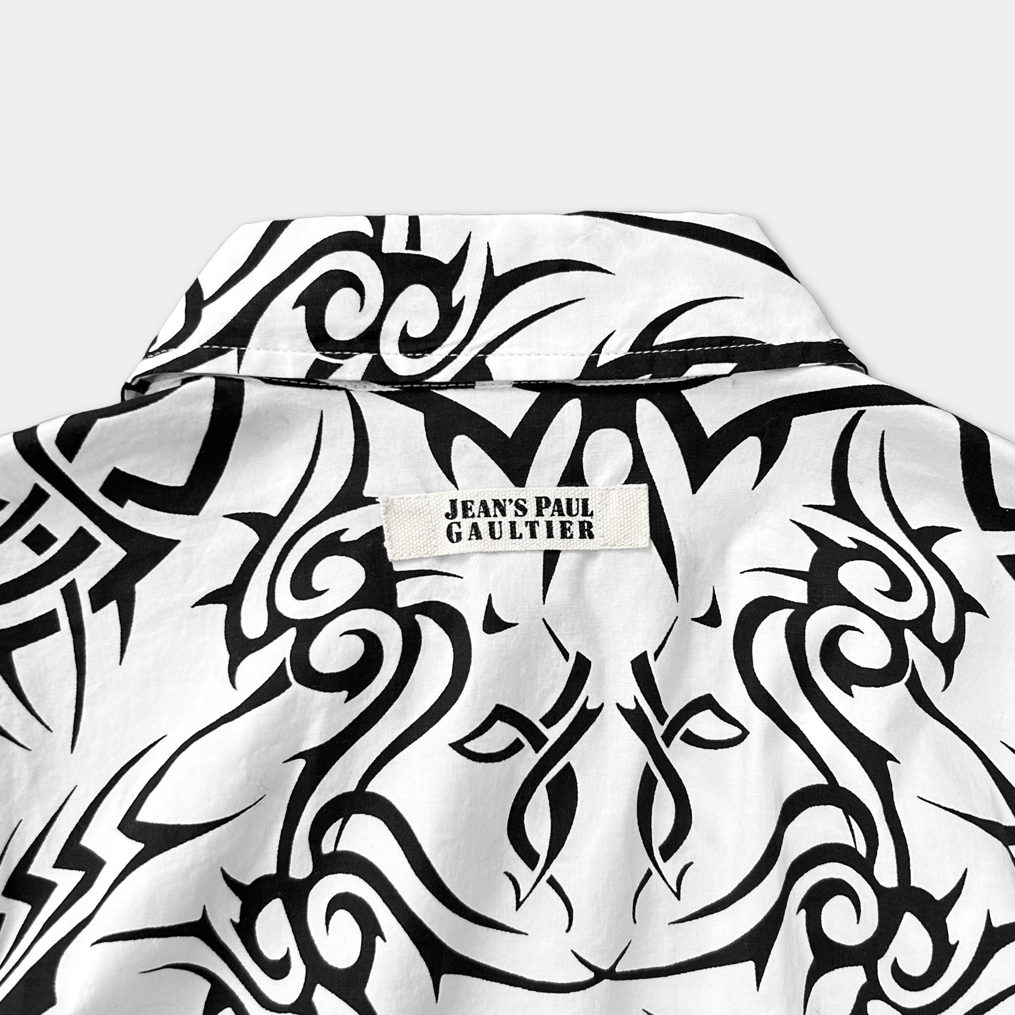 the back of a white shirt with a black and white tribal pattern. There is a label on the shirt that reads "Jean's Paul Gaultier".