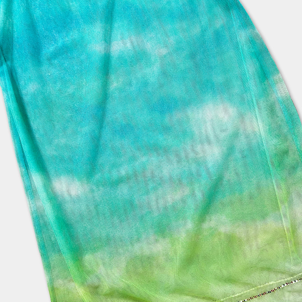 a fabric with a tie-dye pattern, featuring a gradient of green and blue colors. The fabric appears to be a piece of clothing or textile with a unique, colorful design.