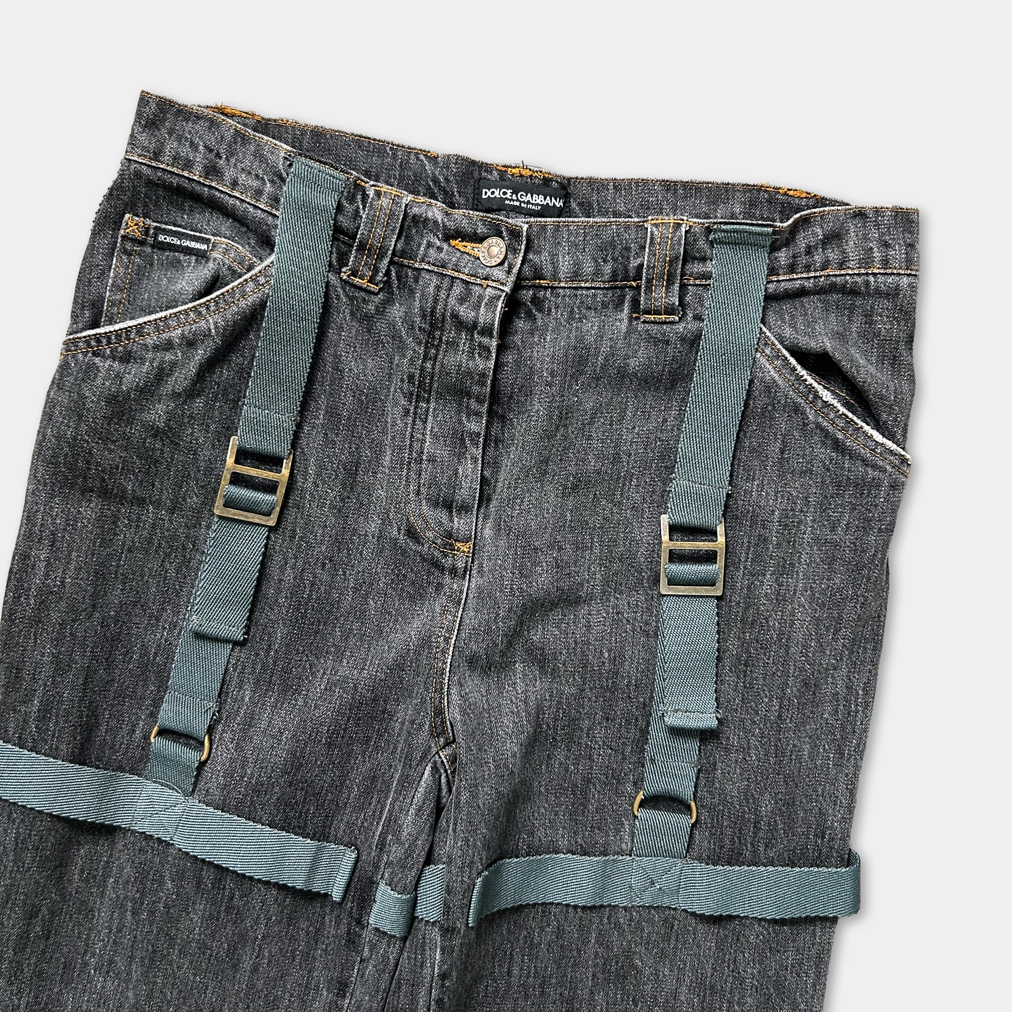 A pair of black jeans with green straps, featuring a label on the waistband.