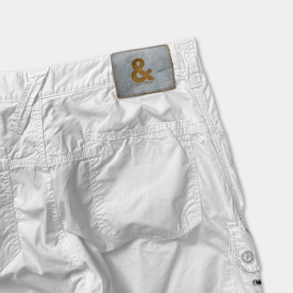 A pair of white shorts with a grey and gold logo on the back pocket.