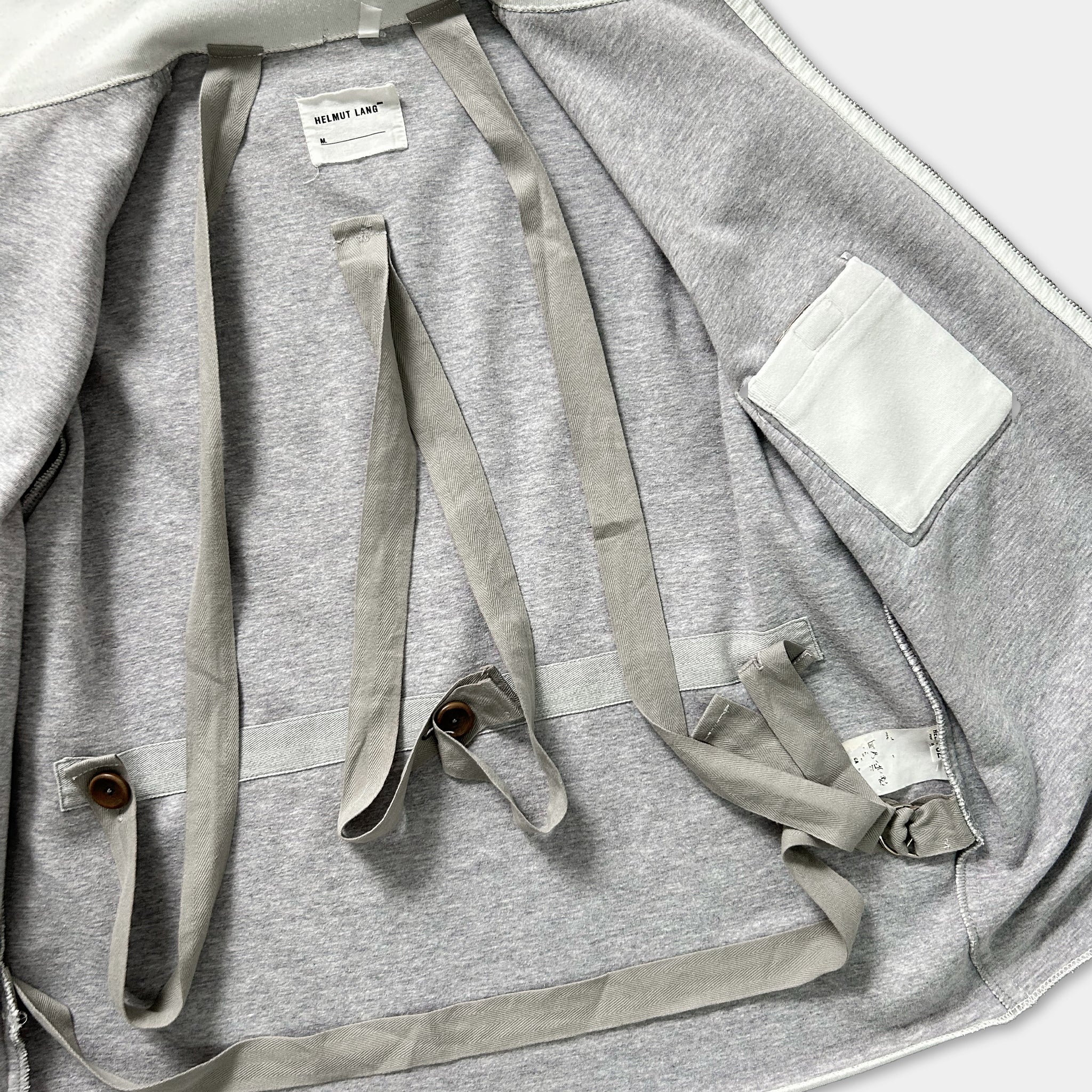 the inside of a gray sweatshirt with a white pocket and a label on the back.