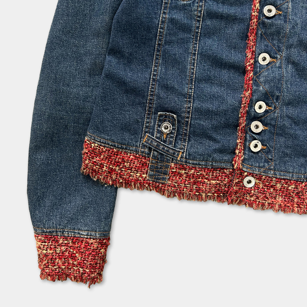 A close-up view of a denim jacket with a red and orange fringe trim, buttons, and a zipper.