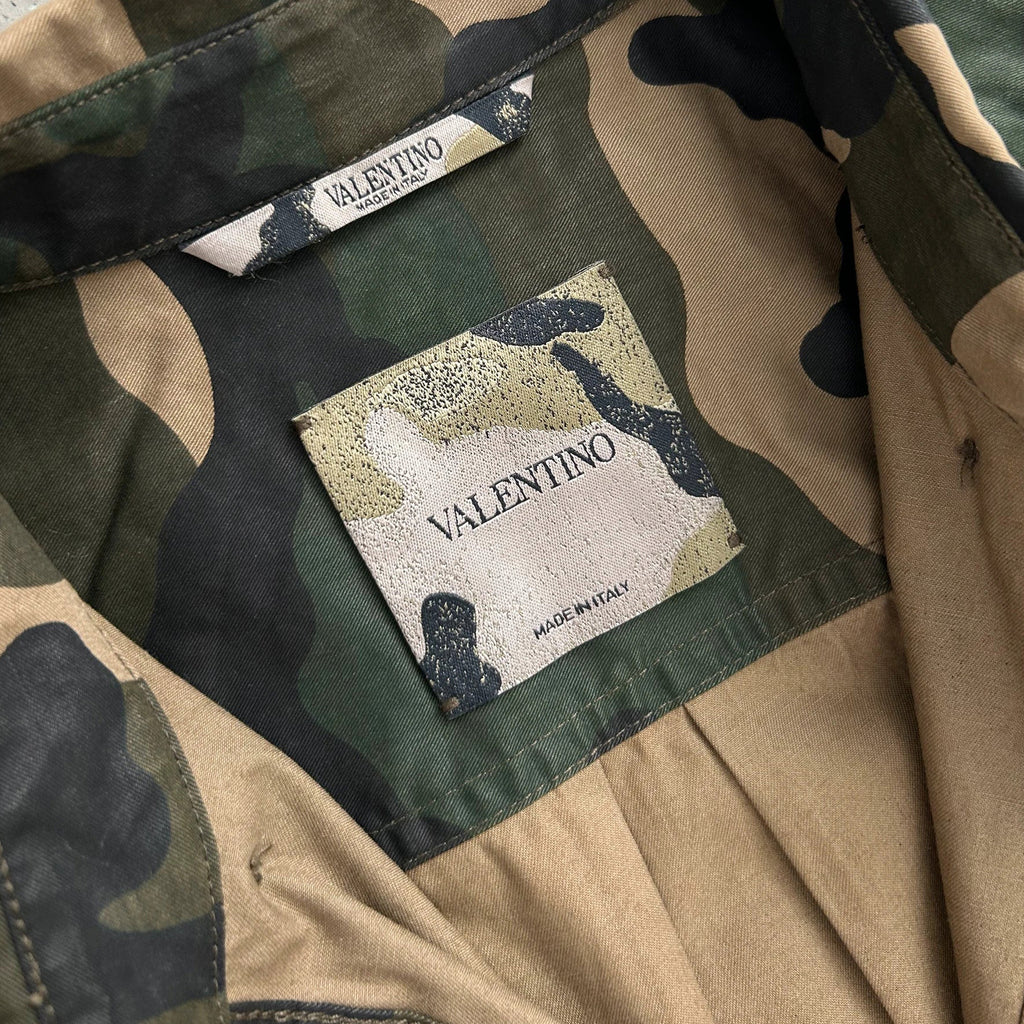a close-up view of a camo-patterned fabric, with a label attached to it that reads "VALENTINO".