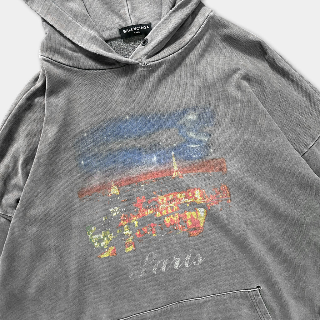 A gray hoodie with a printed design depicting a cityscape and the word "Paris" printed on it.