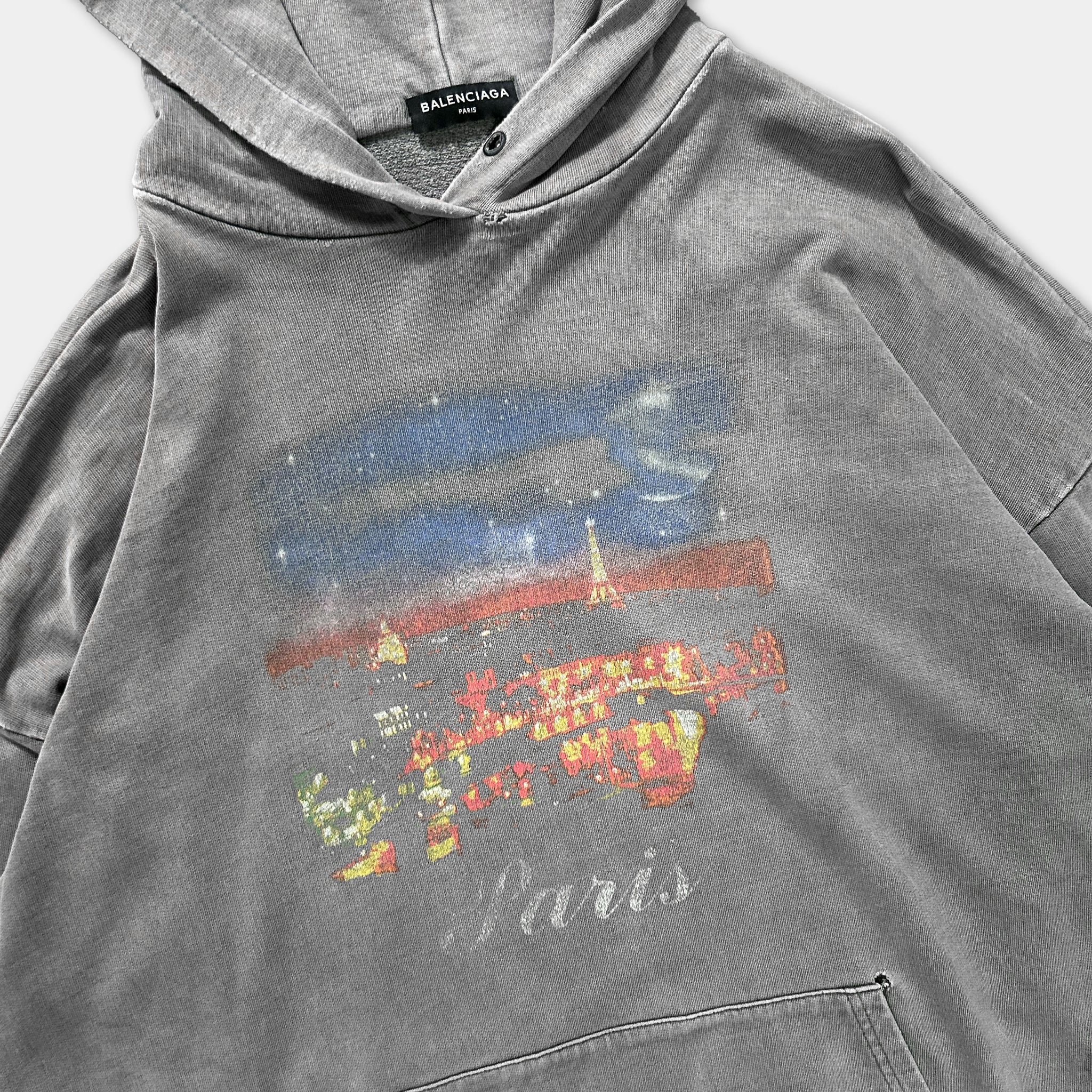 A gray hoodie with a printed design depicting a cityscape and the word "Paris" printed on it.
