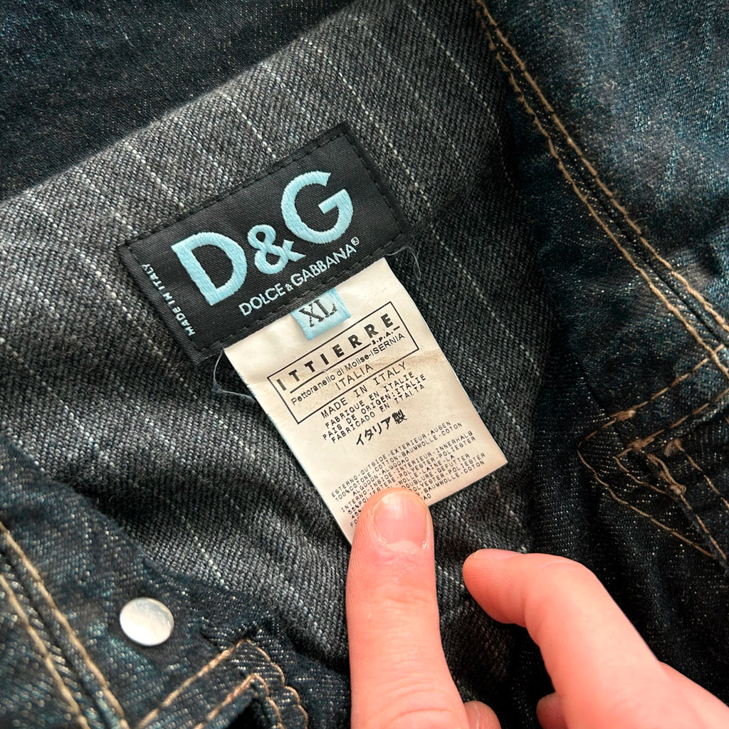 A close-up view of a person's hand holding a D&G denim jeans label, with the label clearly visible.