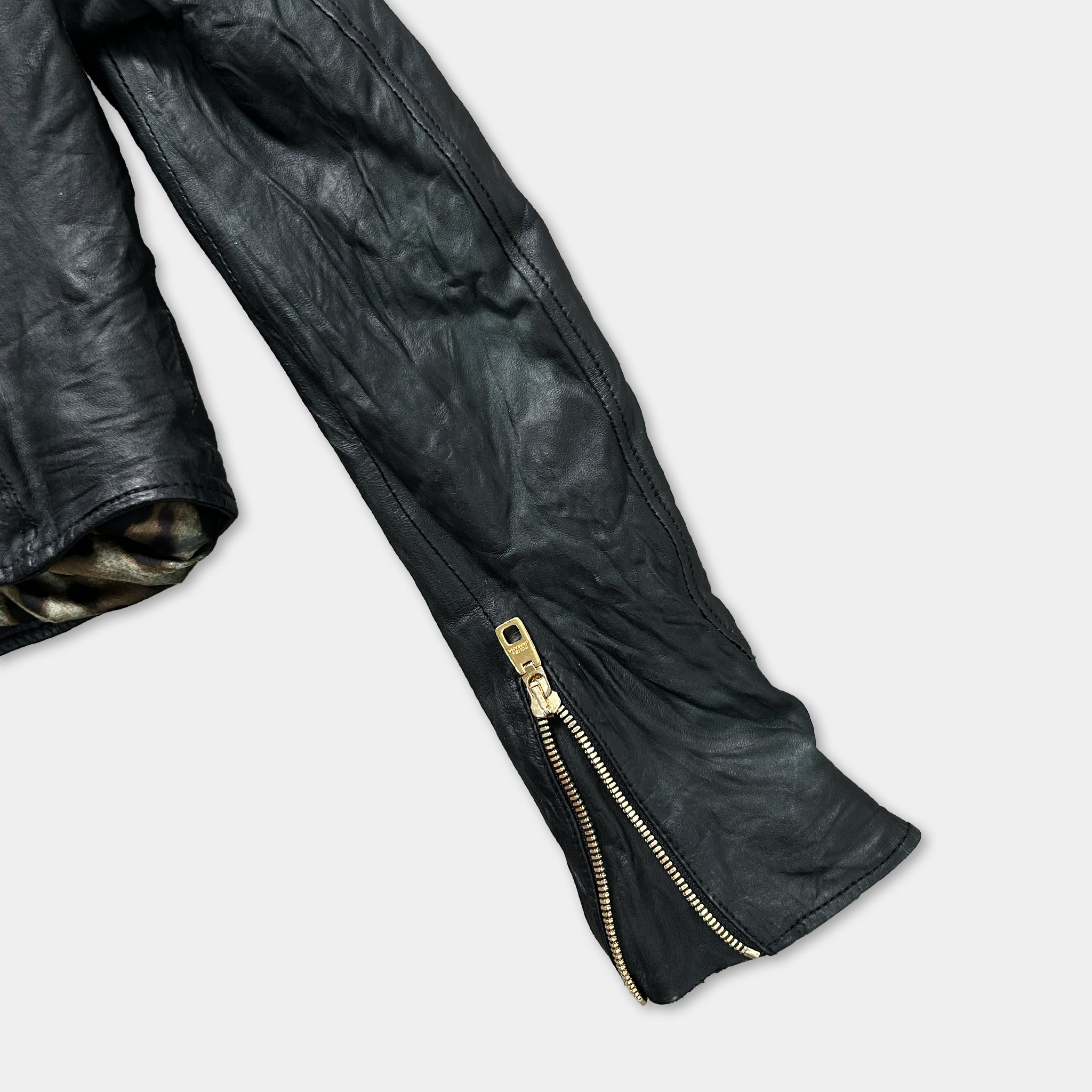 A close-up view of a black leather jacket with a gold zipper.