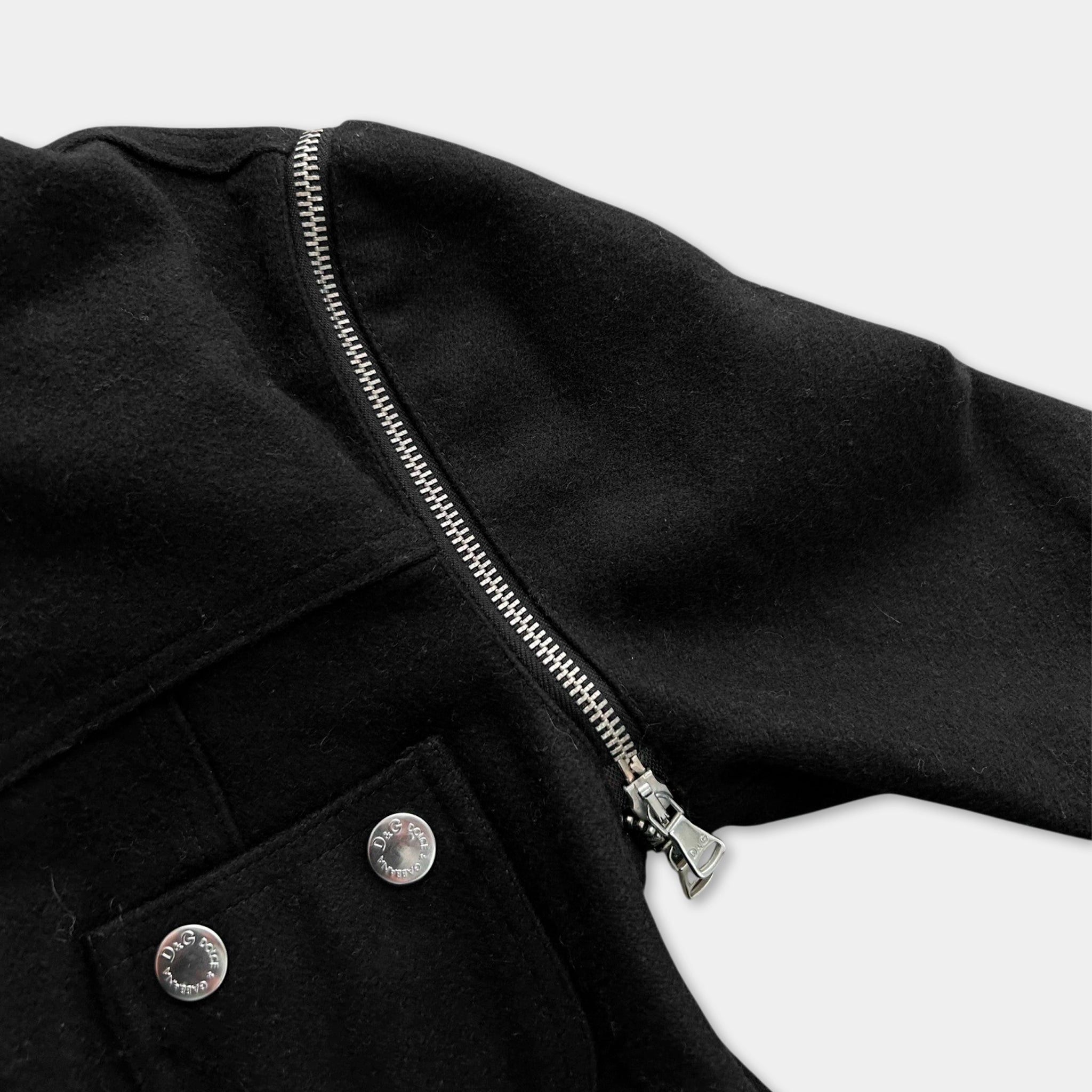 A close-up view of a black jacket with a zipper and two buttons, against a white background.