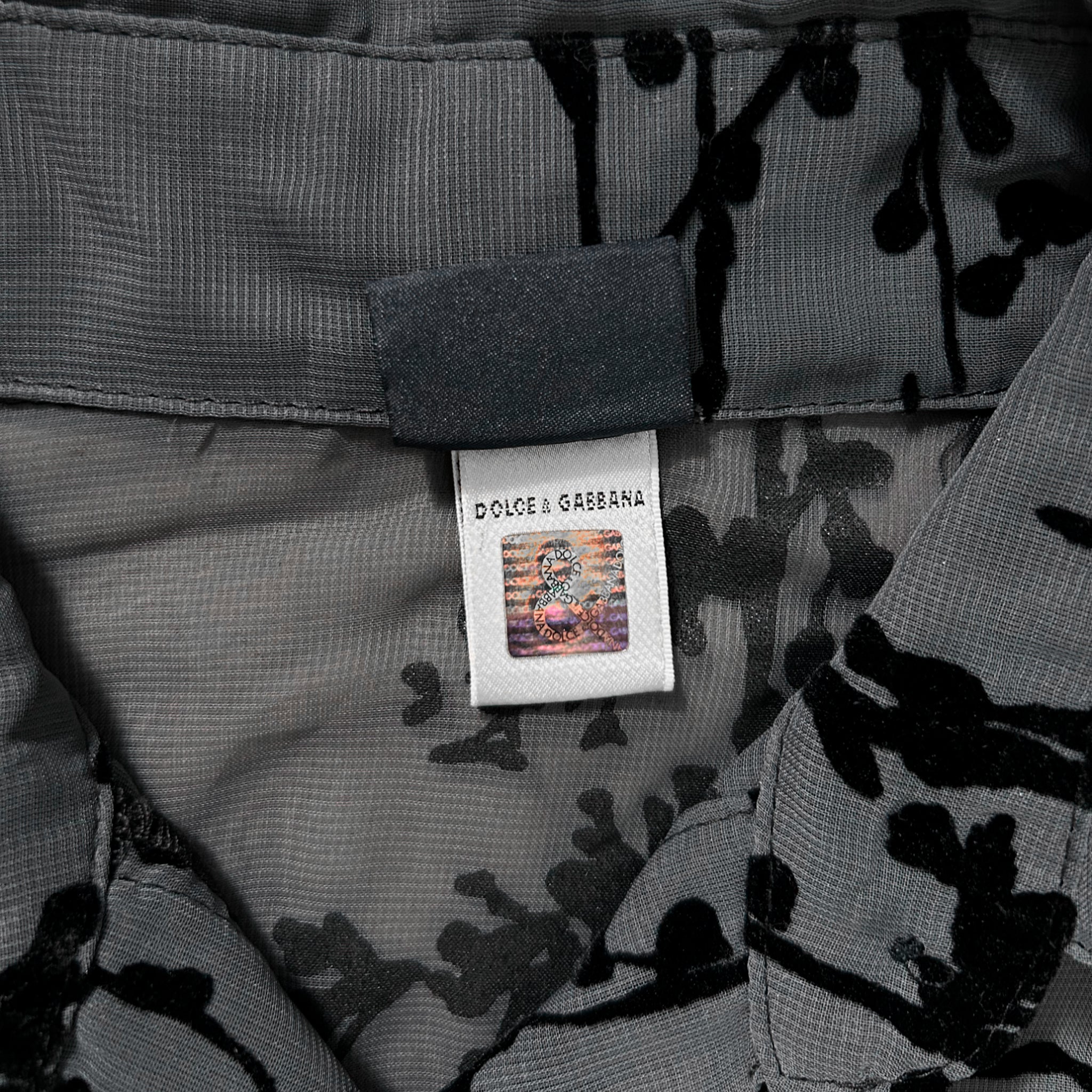 a close-up view of a garment, possibly a shirt or blouse, with a label attached to it. The label appears to be a part of the garment's design, possibly indicating the brand or product information.