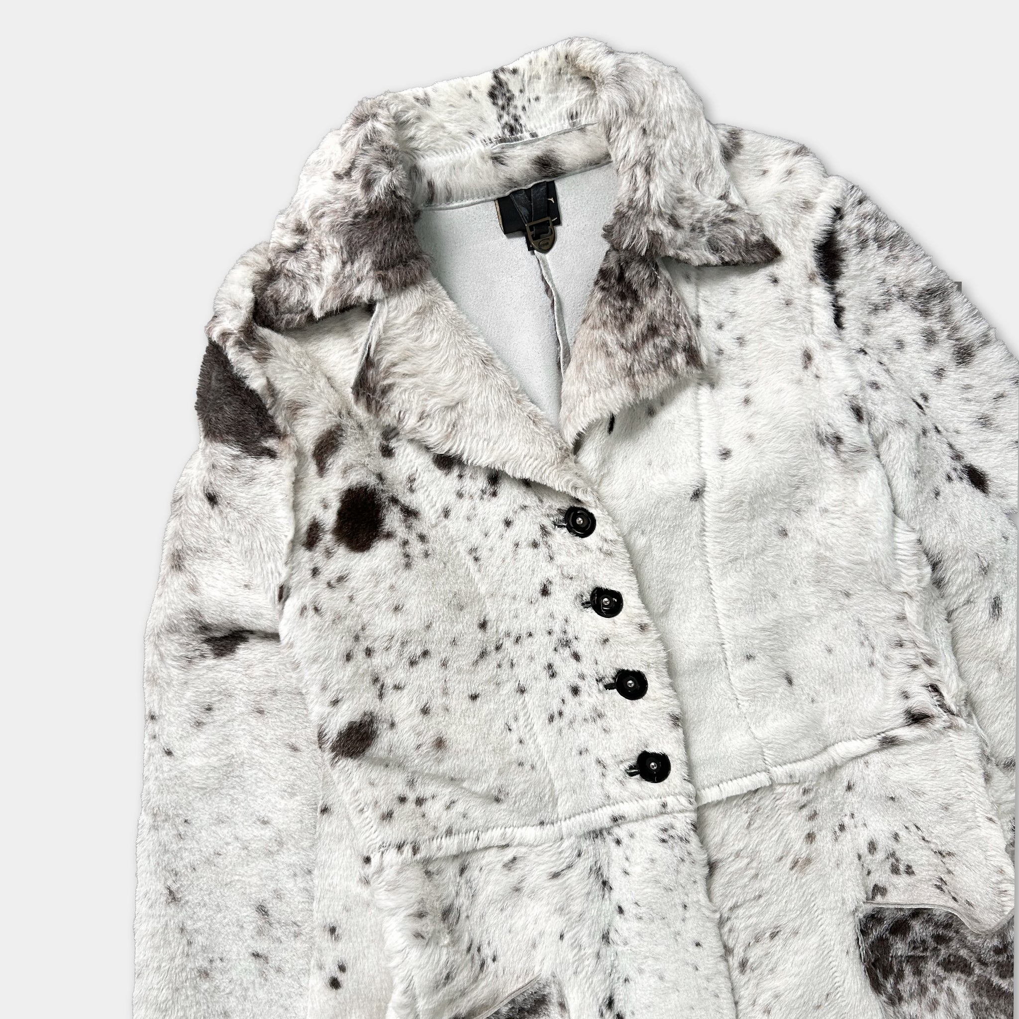 A close-up image of a white fur coat with black spots, featuring a collar, buttons, and a collar.