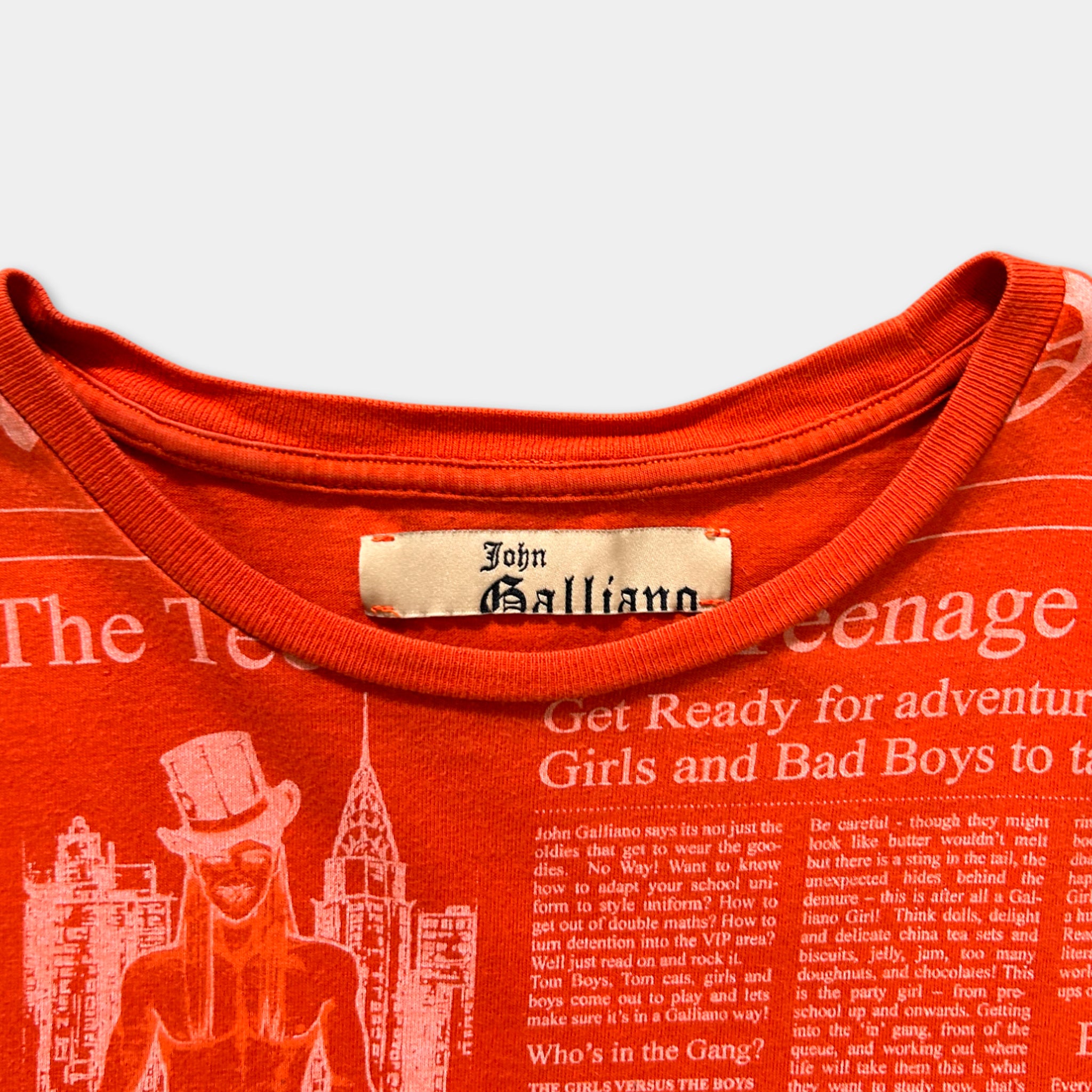 a red t-shirt with a printed label on the collar, featuring a cityscape and a character wearing a top hat.