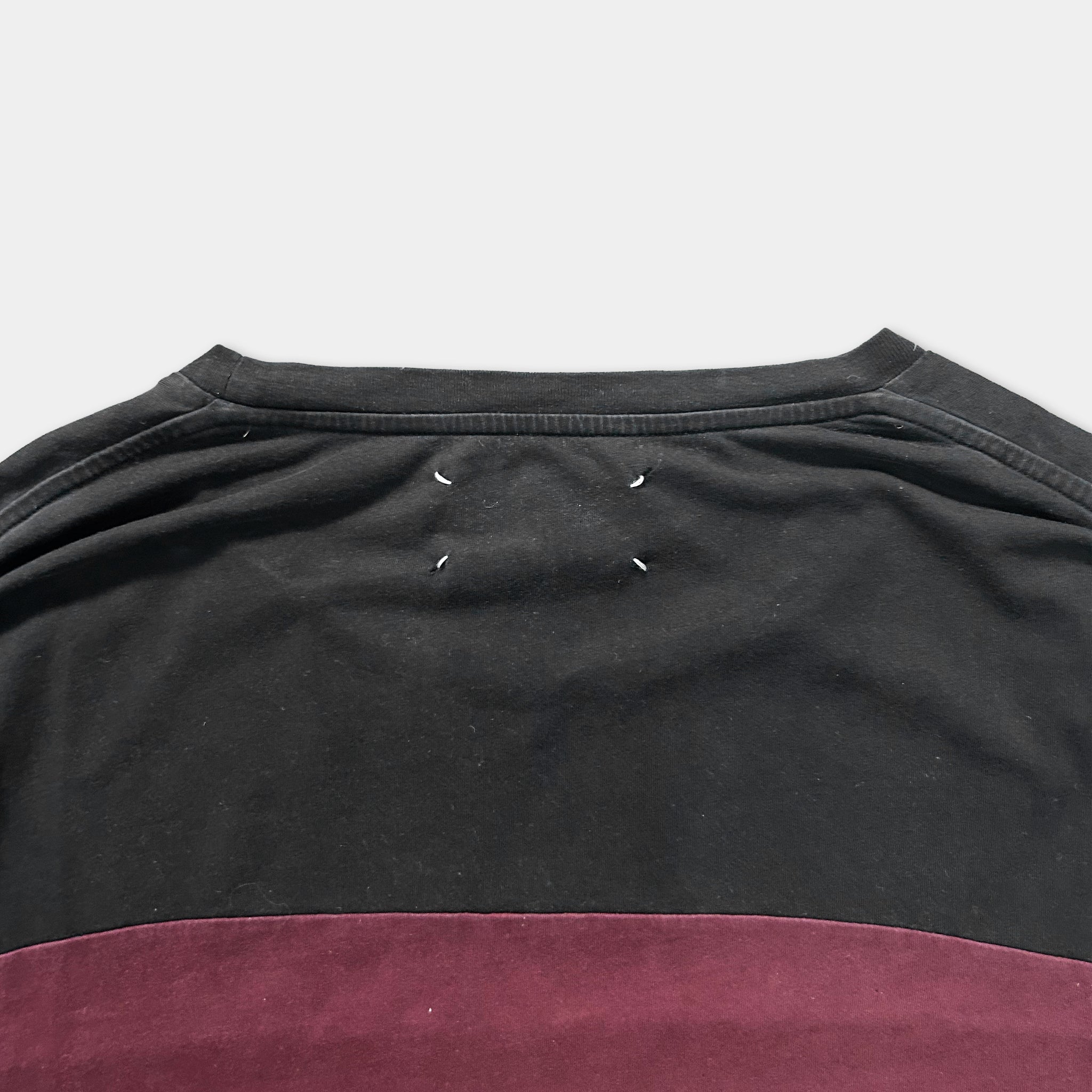a close-up view of the back of a black and red shirt, with a small tear visible on the collar.