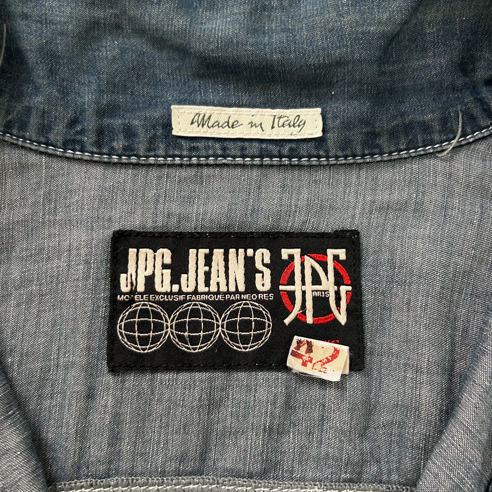a close-up view of a denim jacket, focusing on a label that reads "Made in Italy" and a patch with the initials "JPC.JEAN'S" and a graphic design.