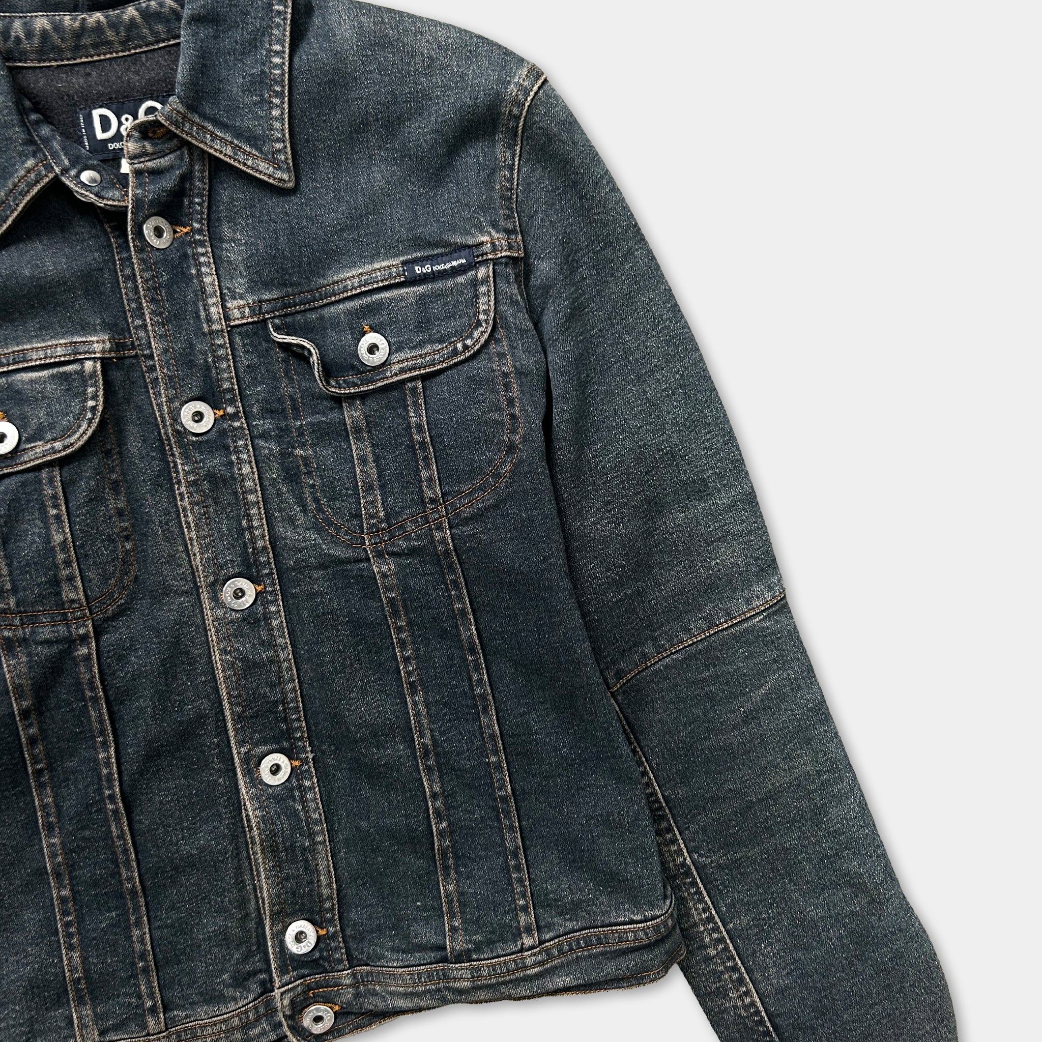 A close-up view of a dark blue denim jacket with a collar, buttons, and pockets.