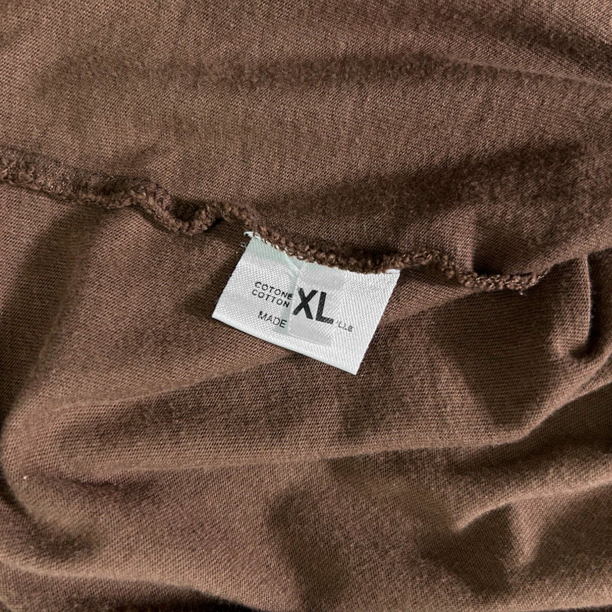 a close-up view of a brown fabric, possibly a shirt or sweater, with a white label attached to it. The label appears to be made of cotton and has the text "XL" printed on it, indicating the size of the garment.