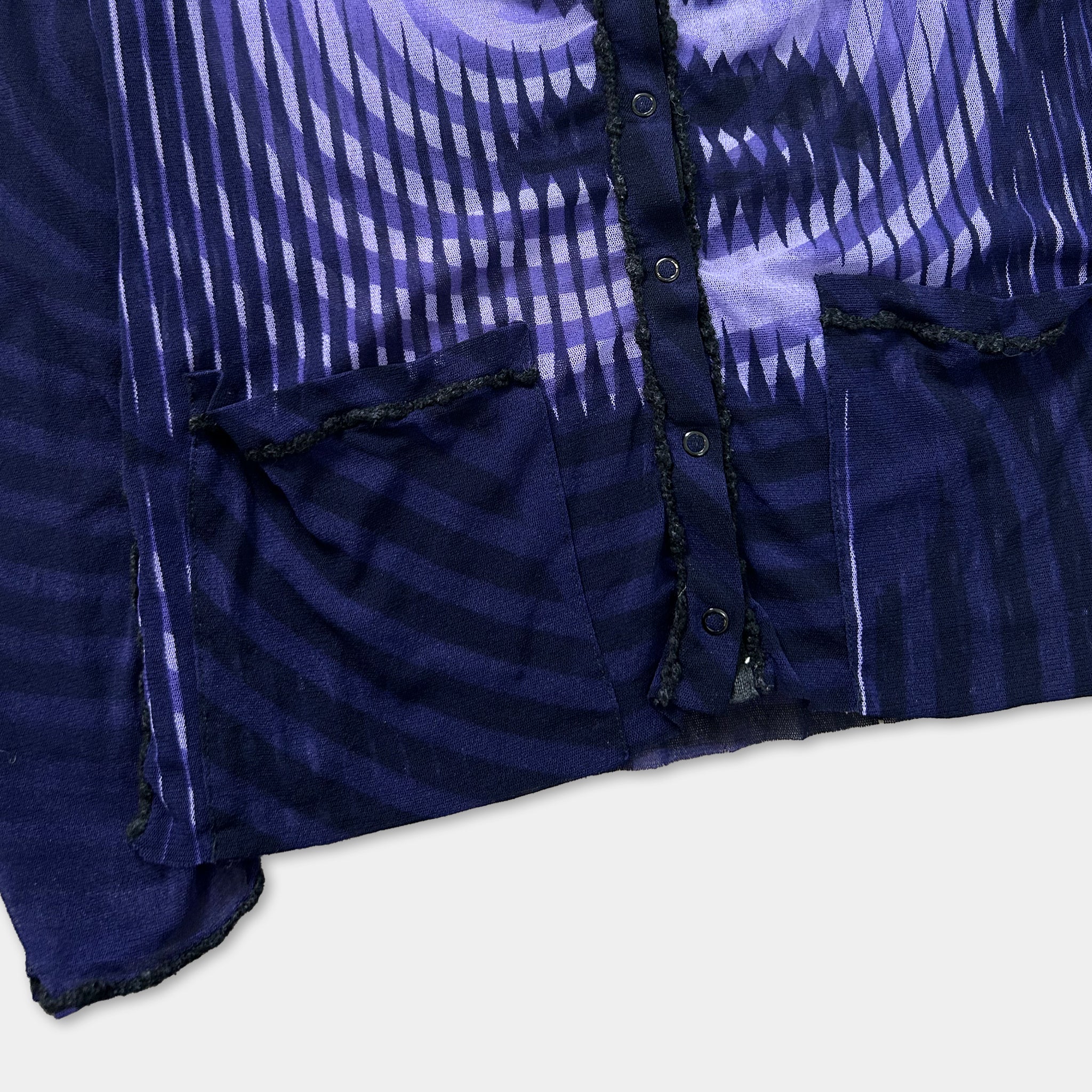 a close-up view of a dark blue fabric with a pattern of purple and white stripes. The fabric appears to be a jacket or cardigan, with a button visible on the front.