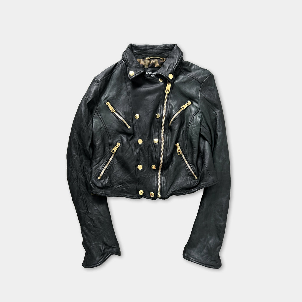 A black leather jacket with gold zippers and buttons, displayed against a white background.