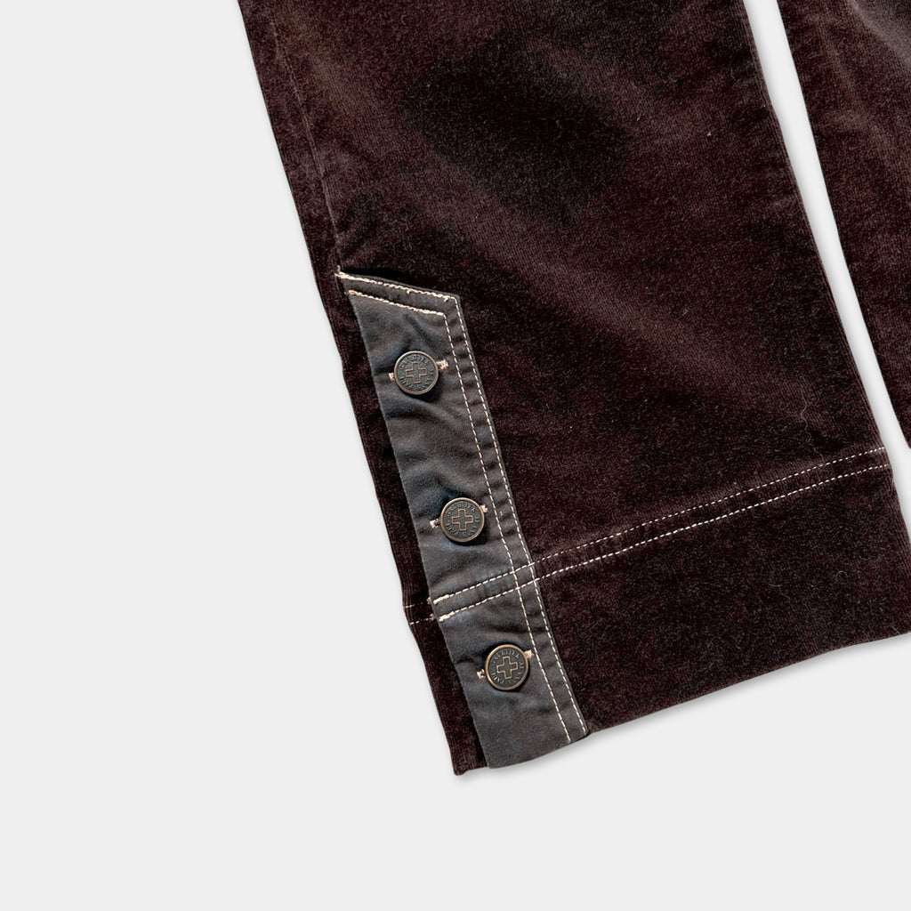 a close-up view of a pair of brown velvet pants with a dark brown pocket and three buttons on the left side.