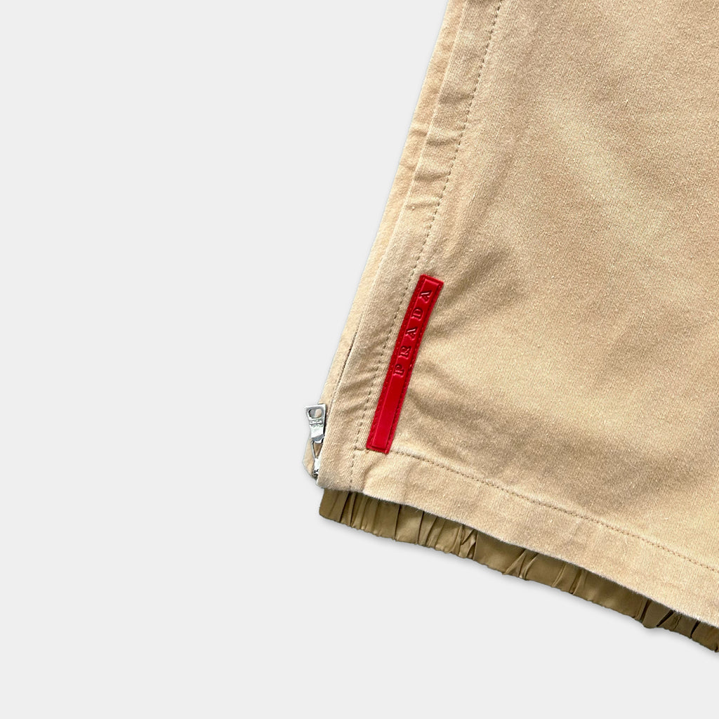 a close-up view of a beige fabric, possibly a piece of clothing, with a red zipper pull visible on the right side.