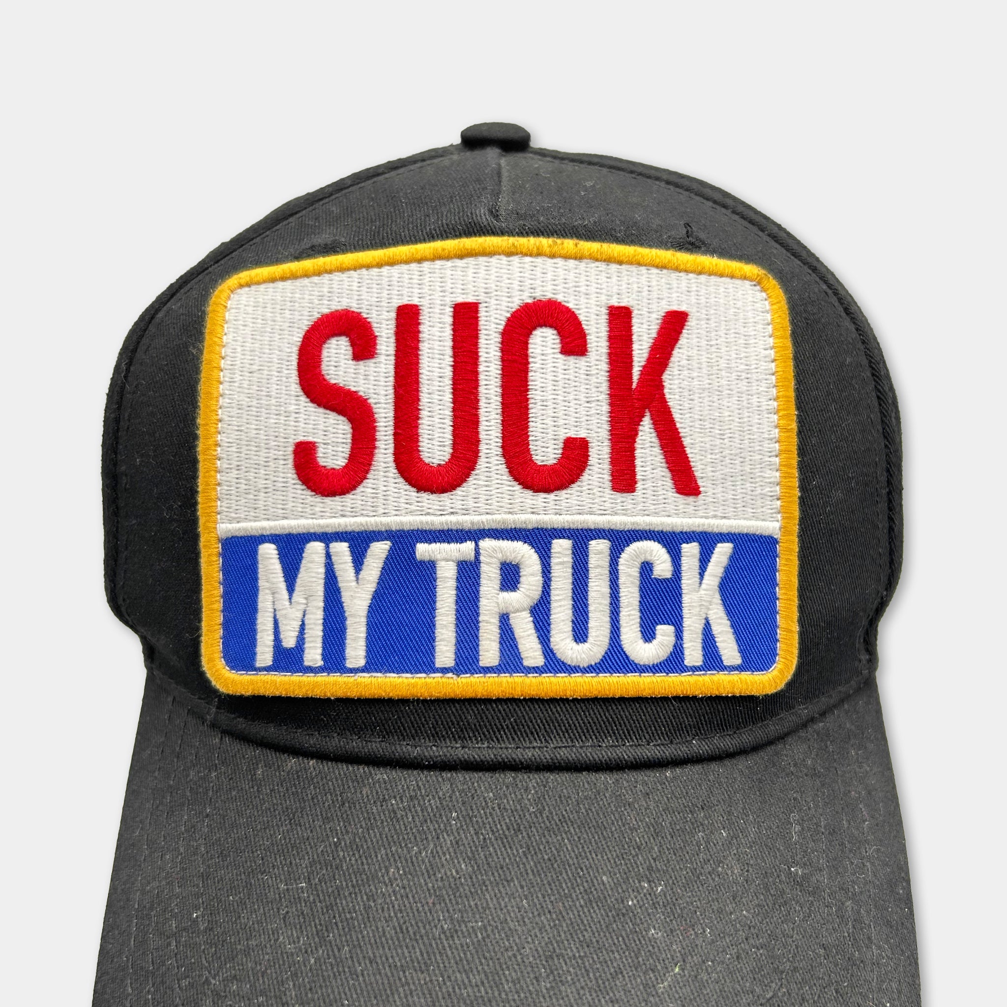 A black baseball cap with a patch on the front that says "SUCK MY TRUCK".