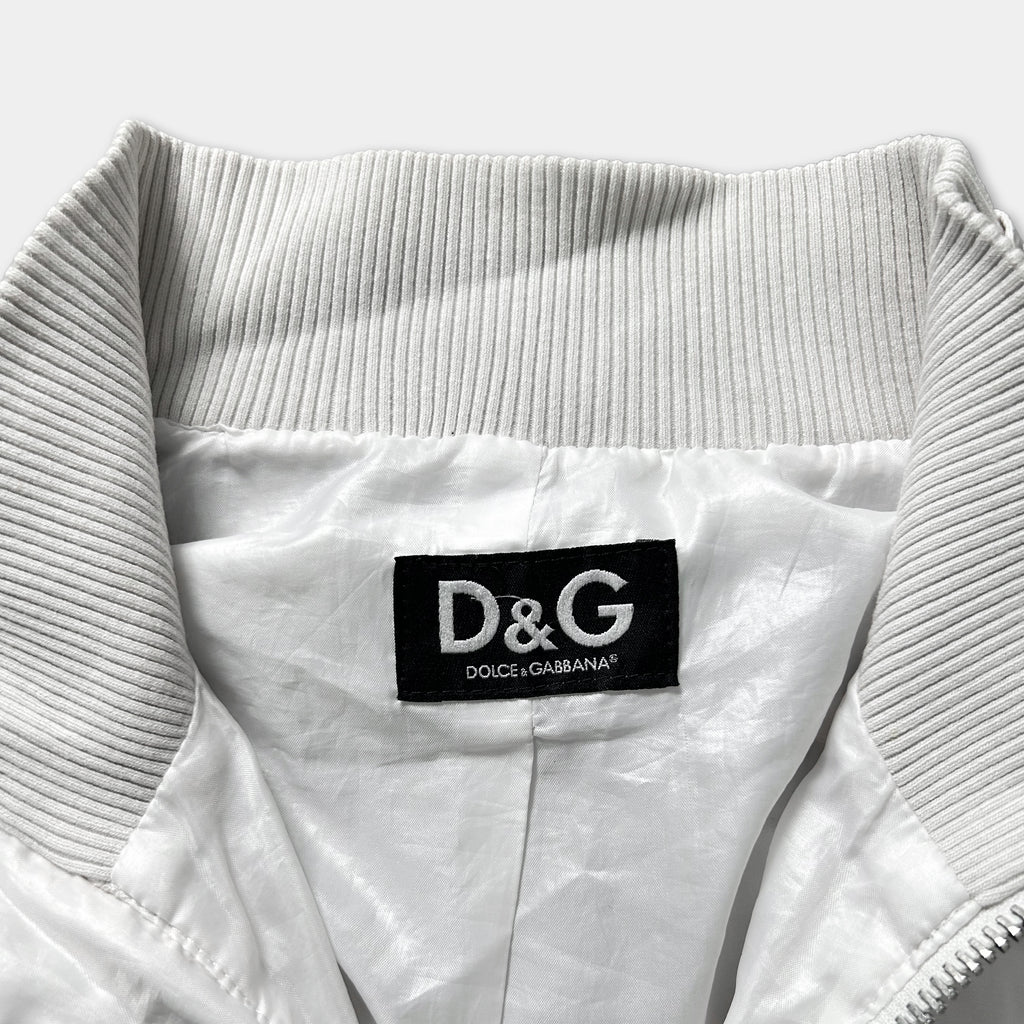 A close-up view of a white jacket collar with a black label displaying the D&G logo and the text "DOLCE&GABBANA".