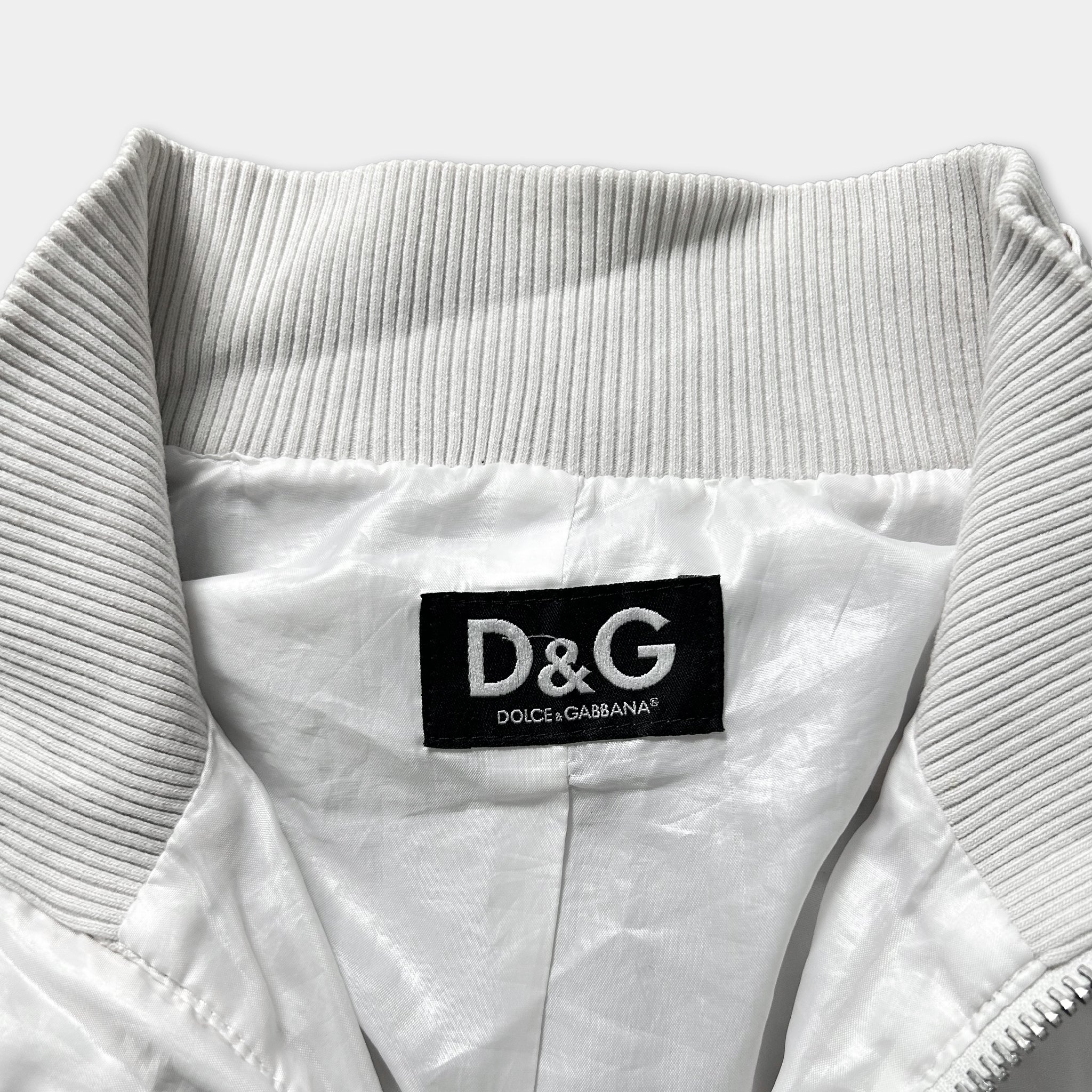 A close-up view of a white jacket collar with a black label displaying the D&G logo and the text "DOLCE&GABBANA".