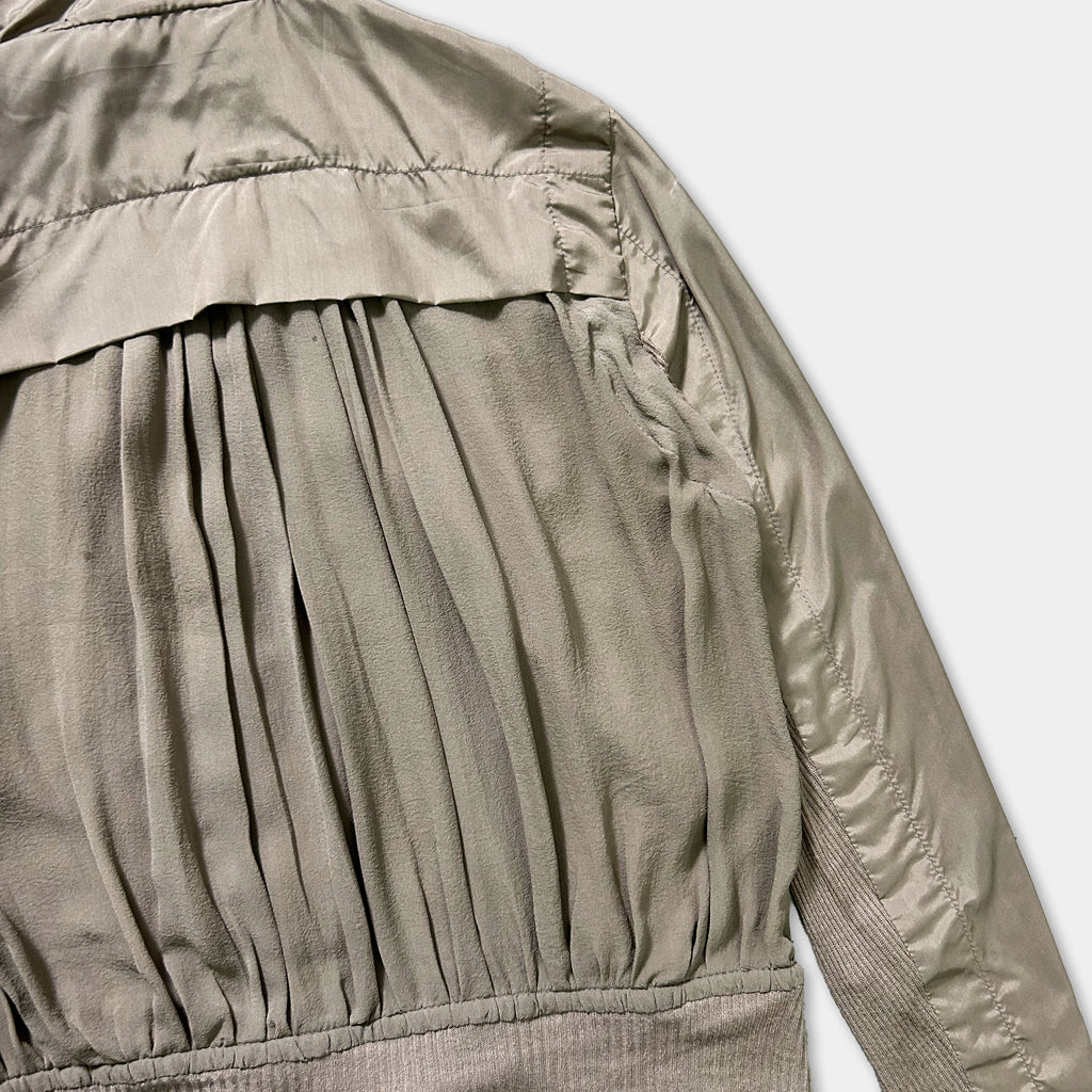 a close-up view of a gray, pleated jacket with a ruffled collar and sleeves.