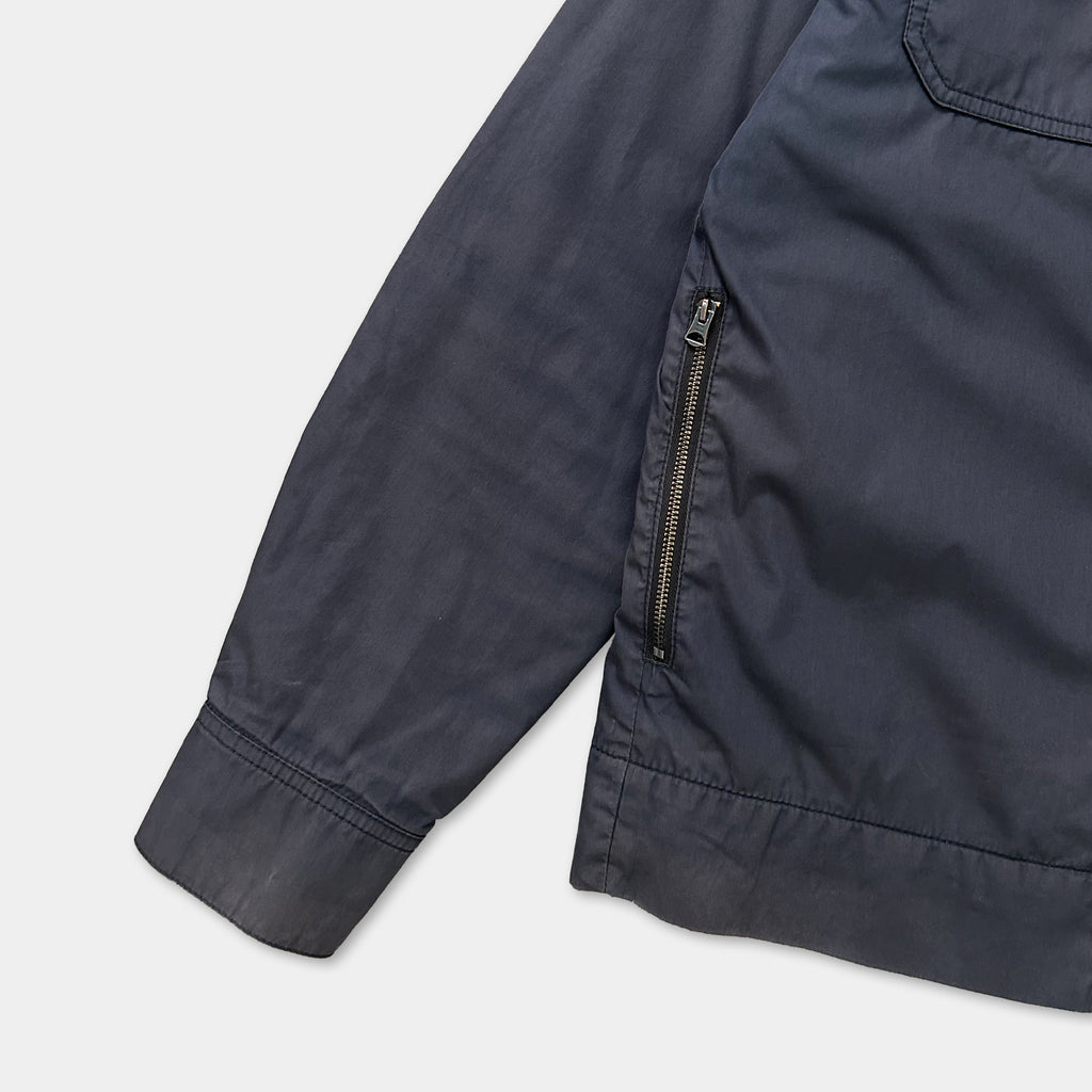 A close-up view of a dark-colored jacket with a zipper and pocket, showing the fabric and details of the garment.