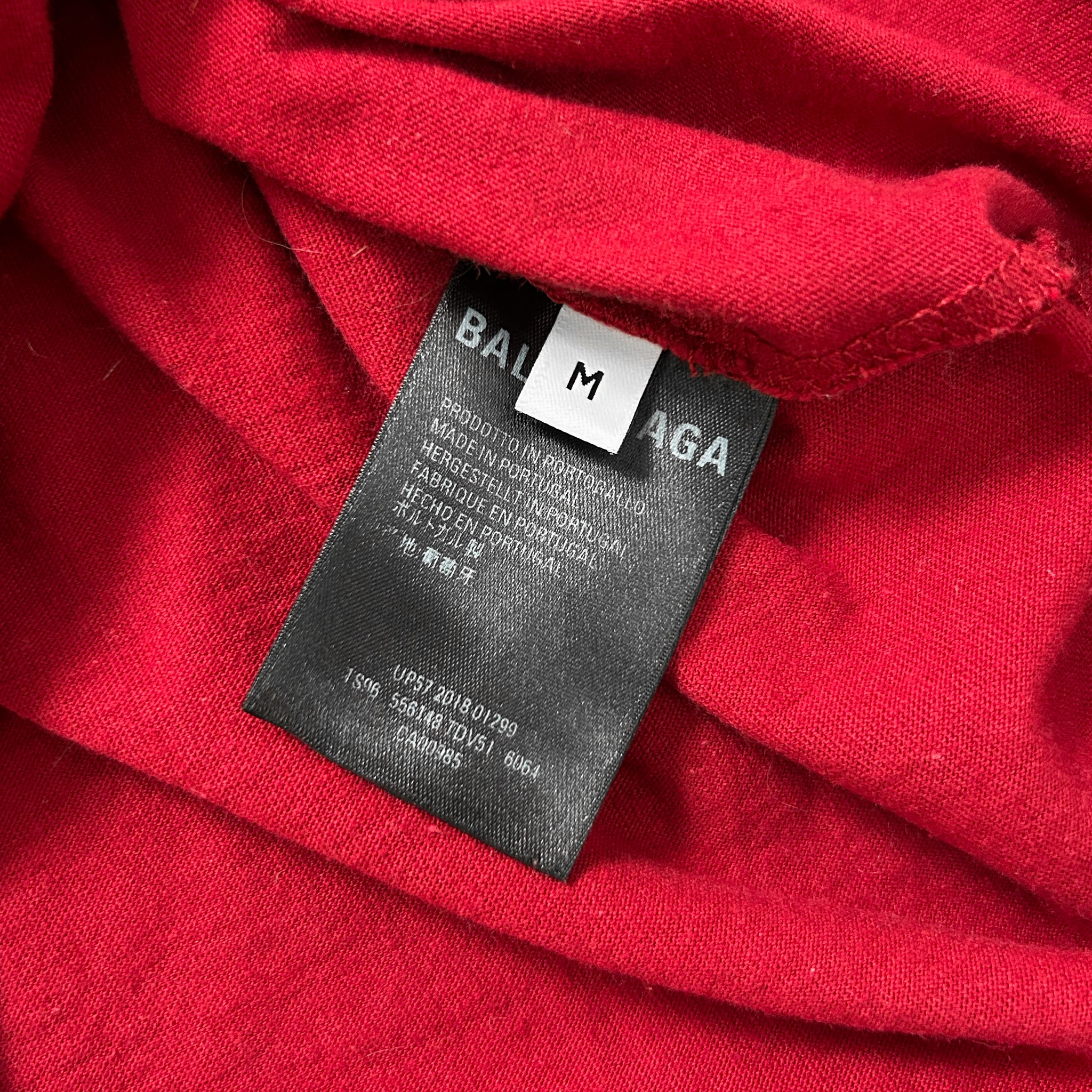 A close-up view of a red fabric with a black label attached to it, displaying text and a barcode.