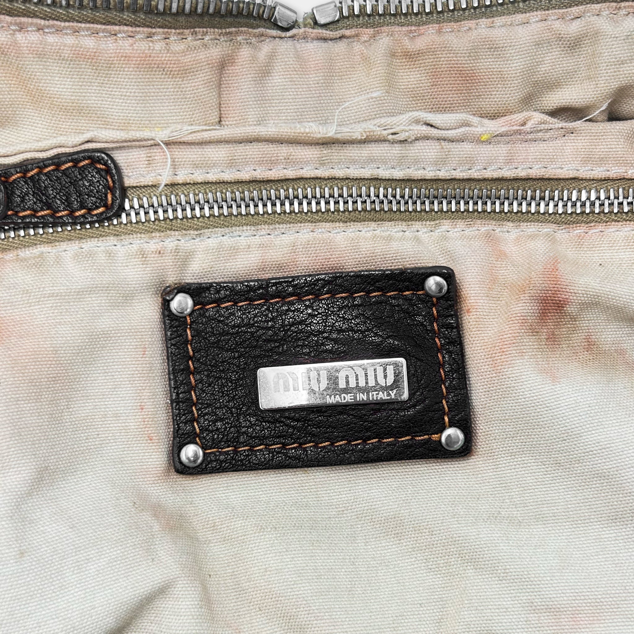a close-up view of a leather tag or label on a fabric material, with the text "Miu Made in Italy" printed on it.