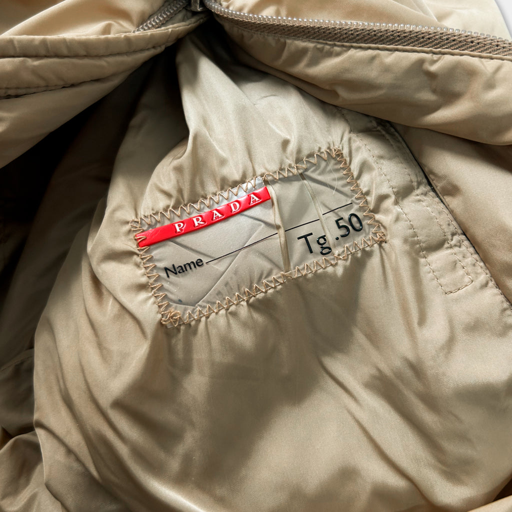 a close-up view of a beige fabric, possibly a jacket or sweater, with a red label attached to it. The label appears to be a name tag or a label with a price tag, indicating the brand and price of the item.