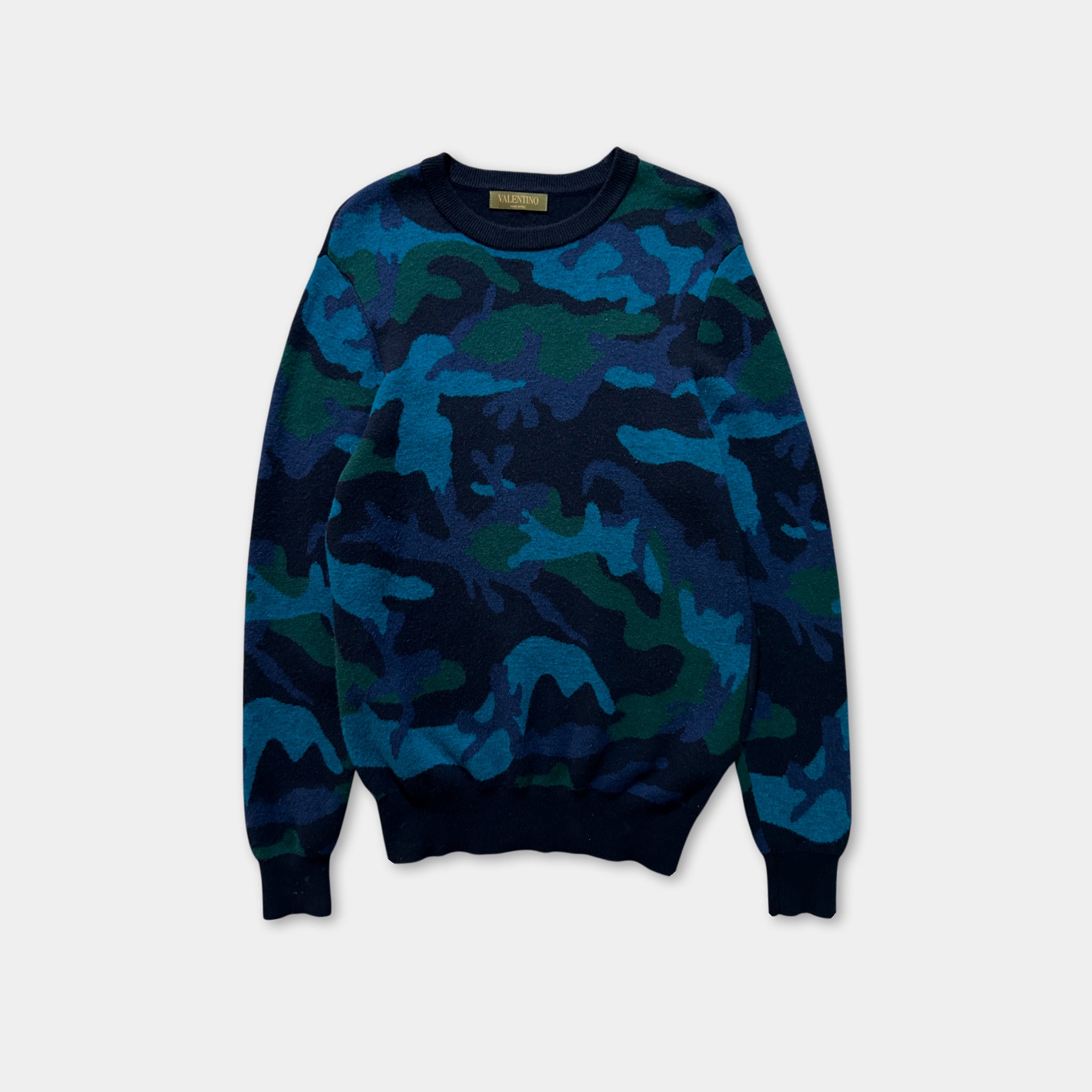 A camouflage-patterned long-sleeved sweater is displayed against a white background.