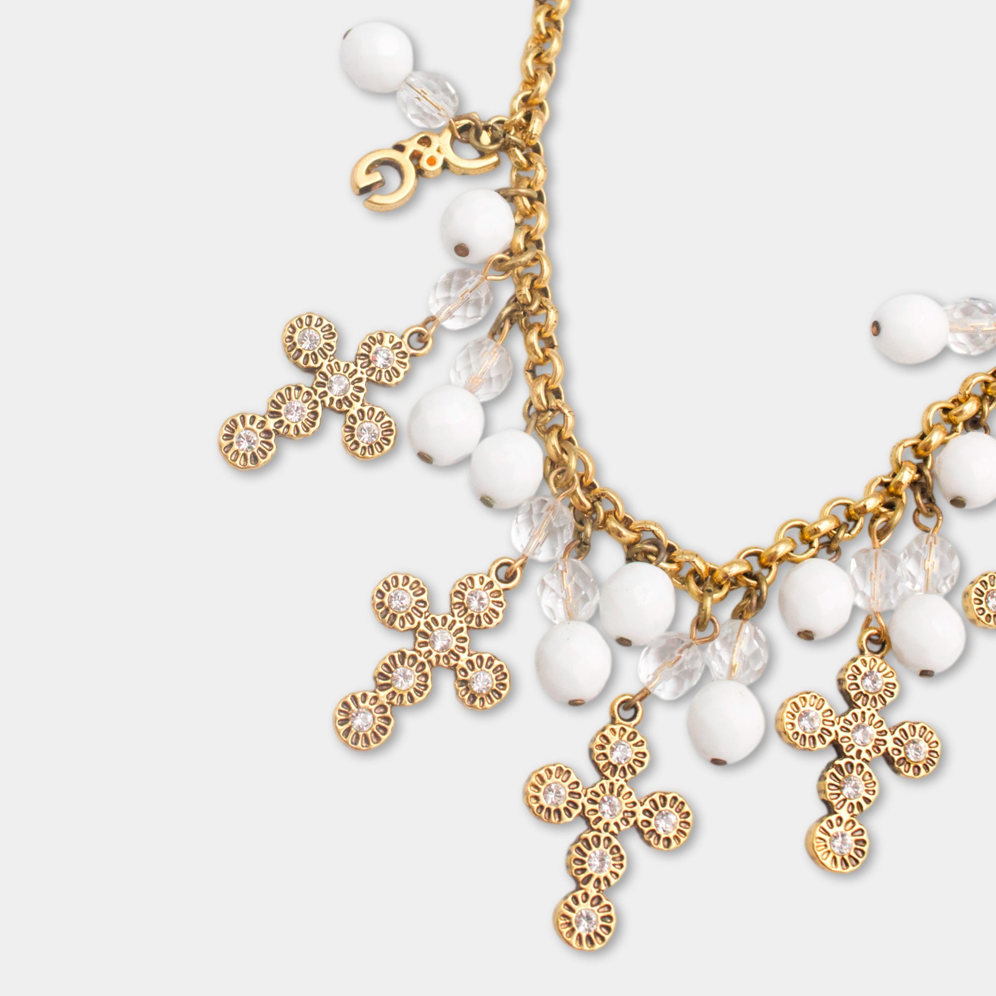 A gold-colored necklace with a cross-shaped pendant and white beads hanging from it.
