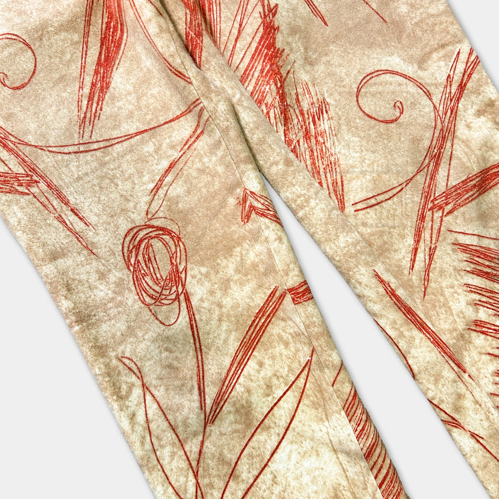 a close-up view of a pair of beige pants with red, abstract designs or lines on the fabric.