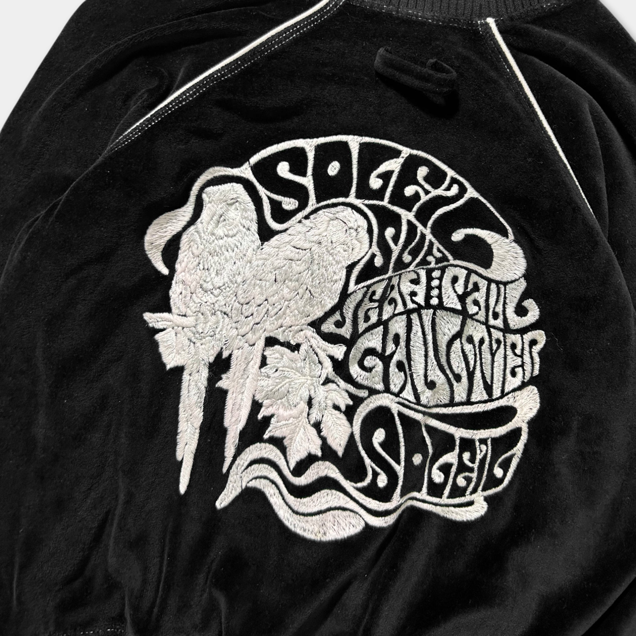 a close-up view of a black velvet jacket with a white embroidered design on the back. The design includes a stylized bird and the text "Sole & the Sea" in a decorative font.
