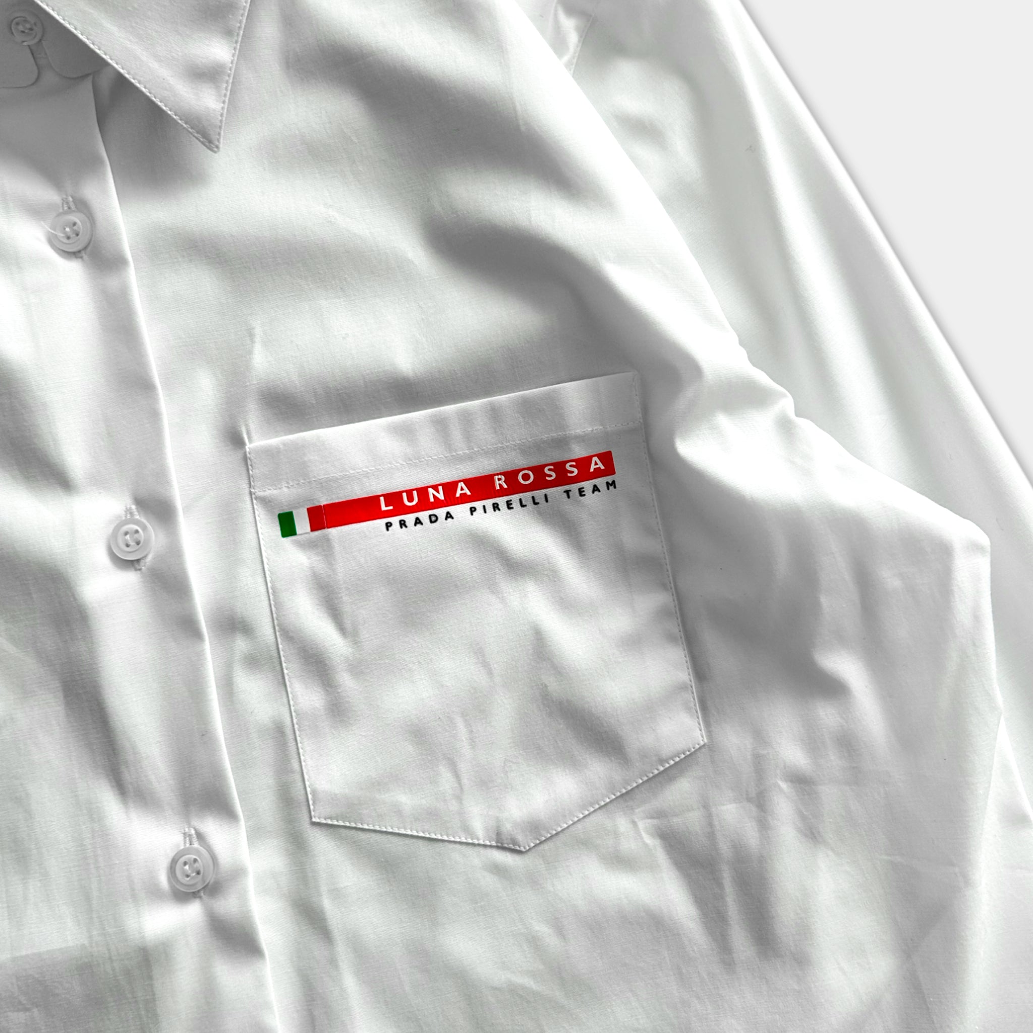 A white shirt with a red and green logo on the left side of the pocket.
