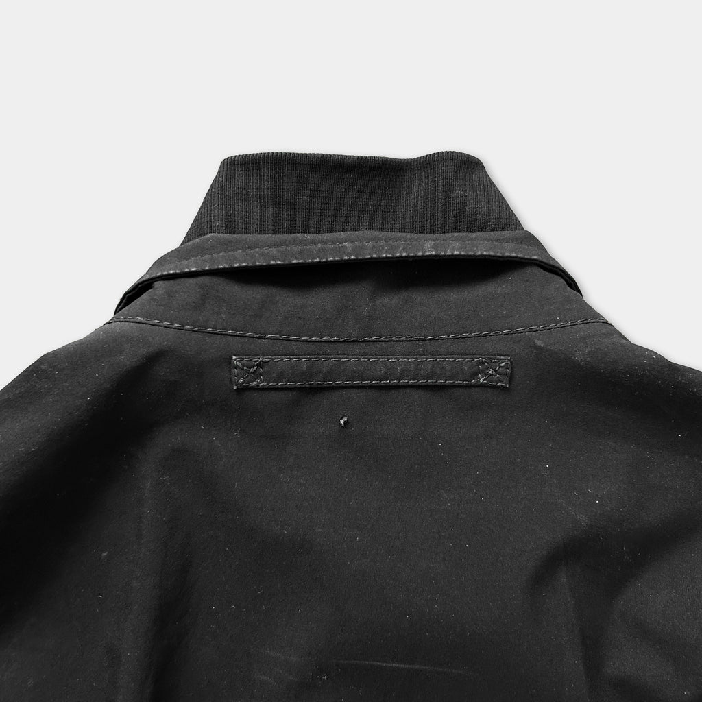 the back of a black jacket or coat, with a zipper and a pocket visible.