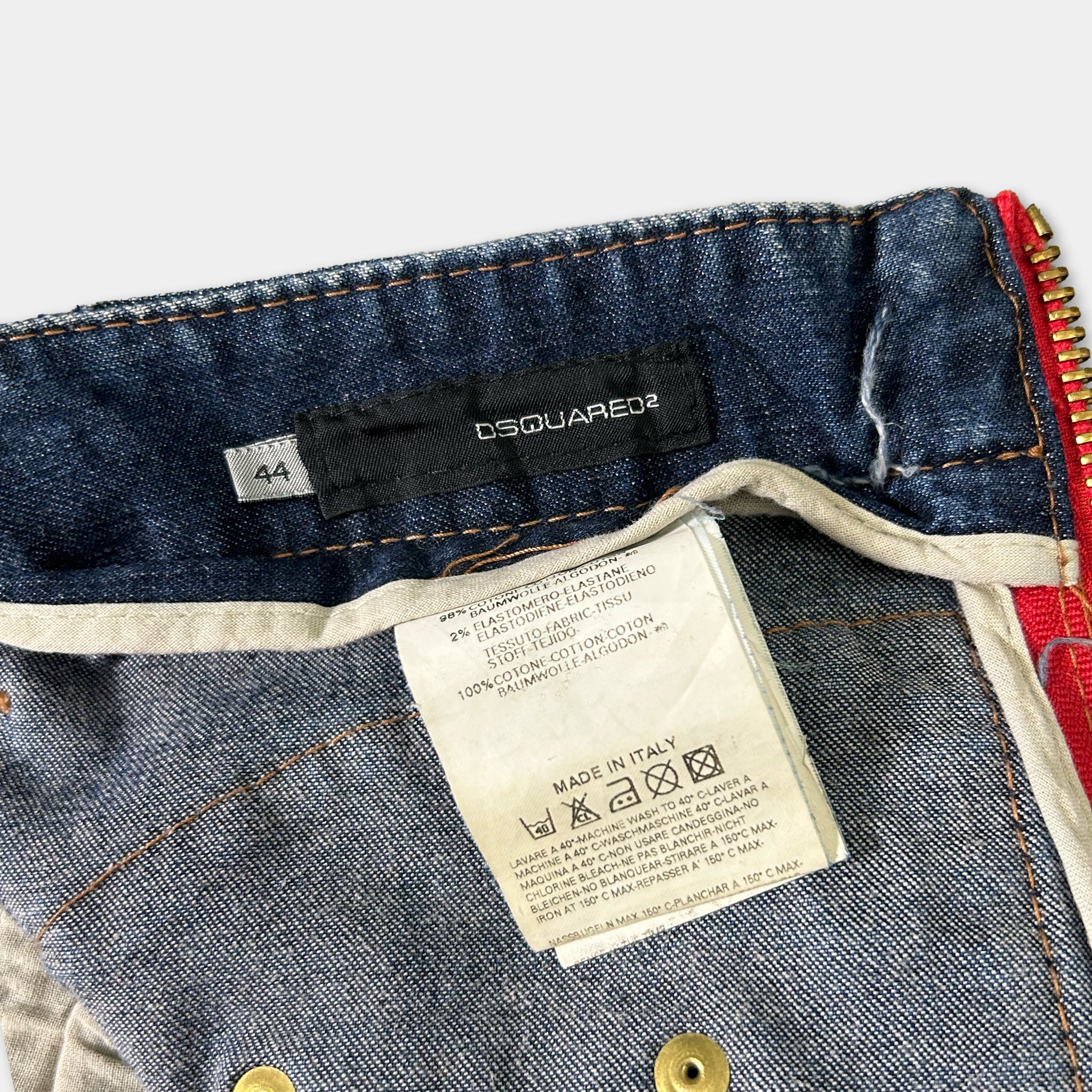 A close-up view of a pair of blue jeans with a label attached to the waistband, indicating the brand and possibly the material or care instructions.