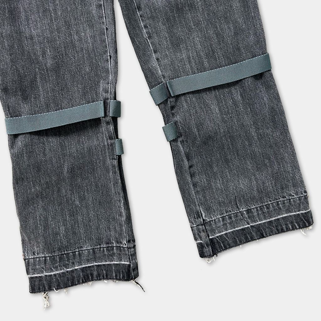 A pair of black jeans with a green strap across the top.