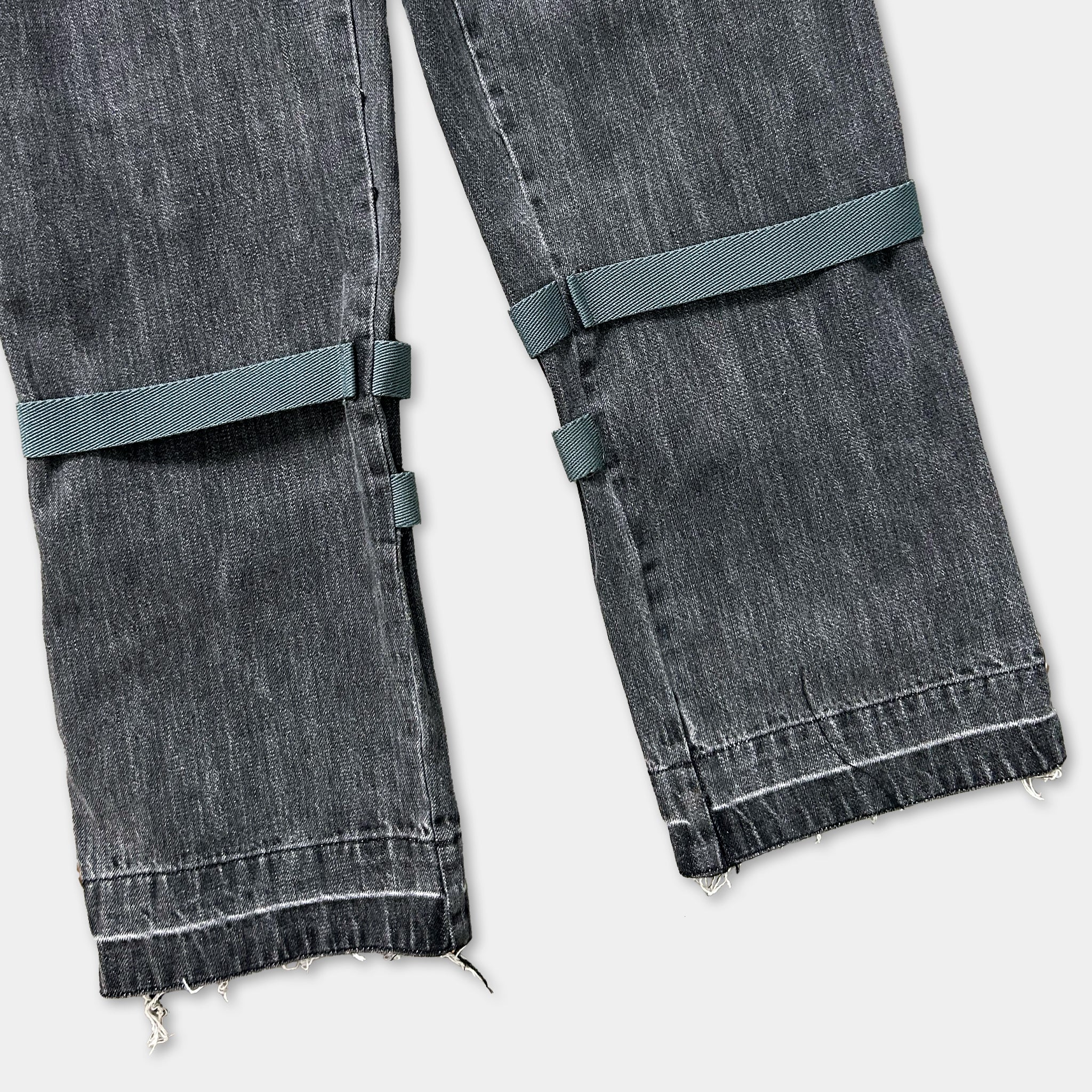 A pair of black jeans with a green strap across the top.