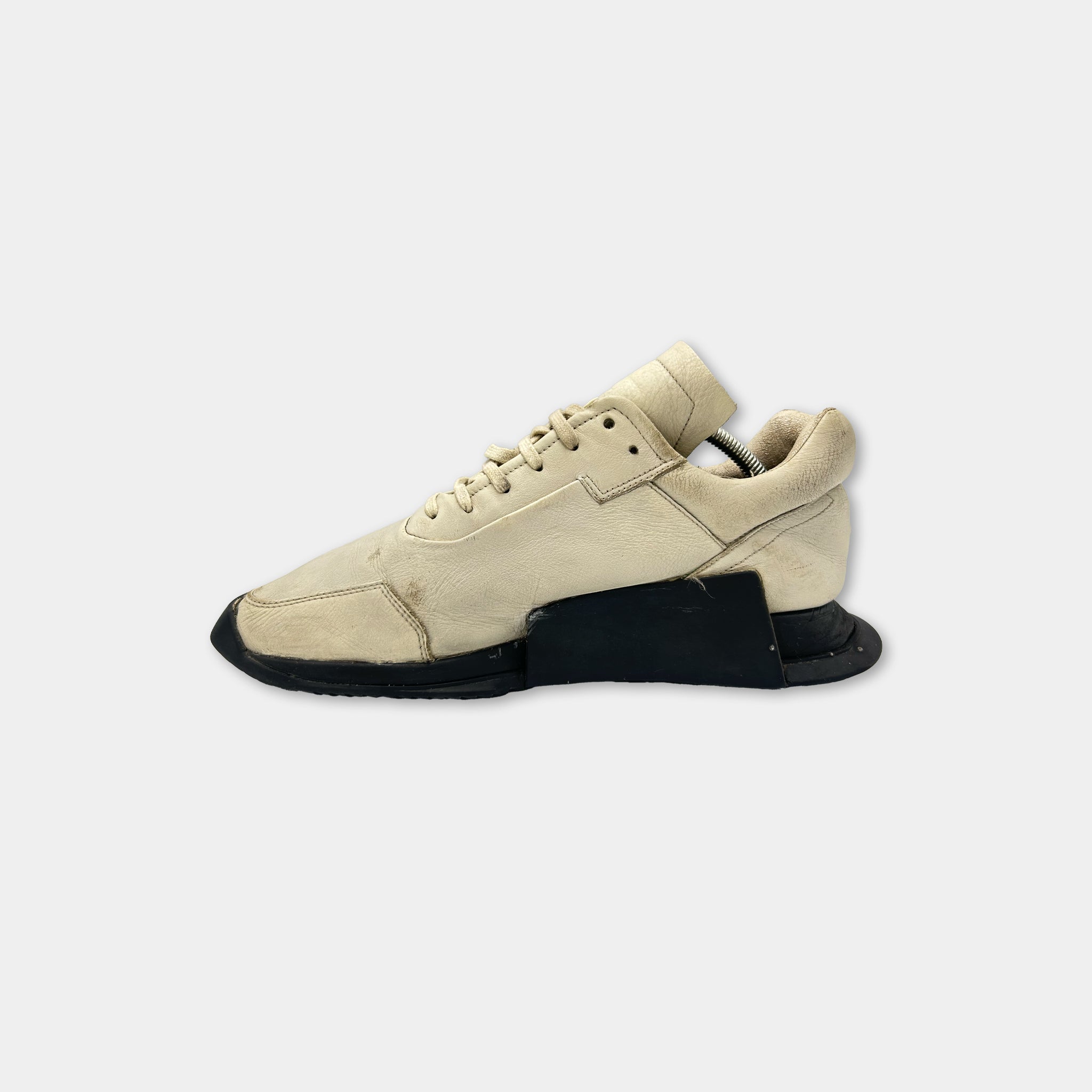 A single beige sneaker with black accents, including the sole and laces, is shown against a white background.