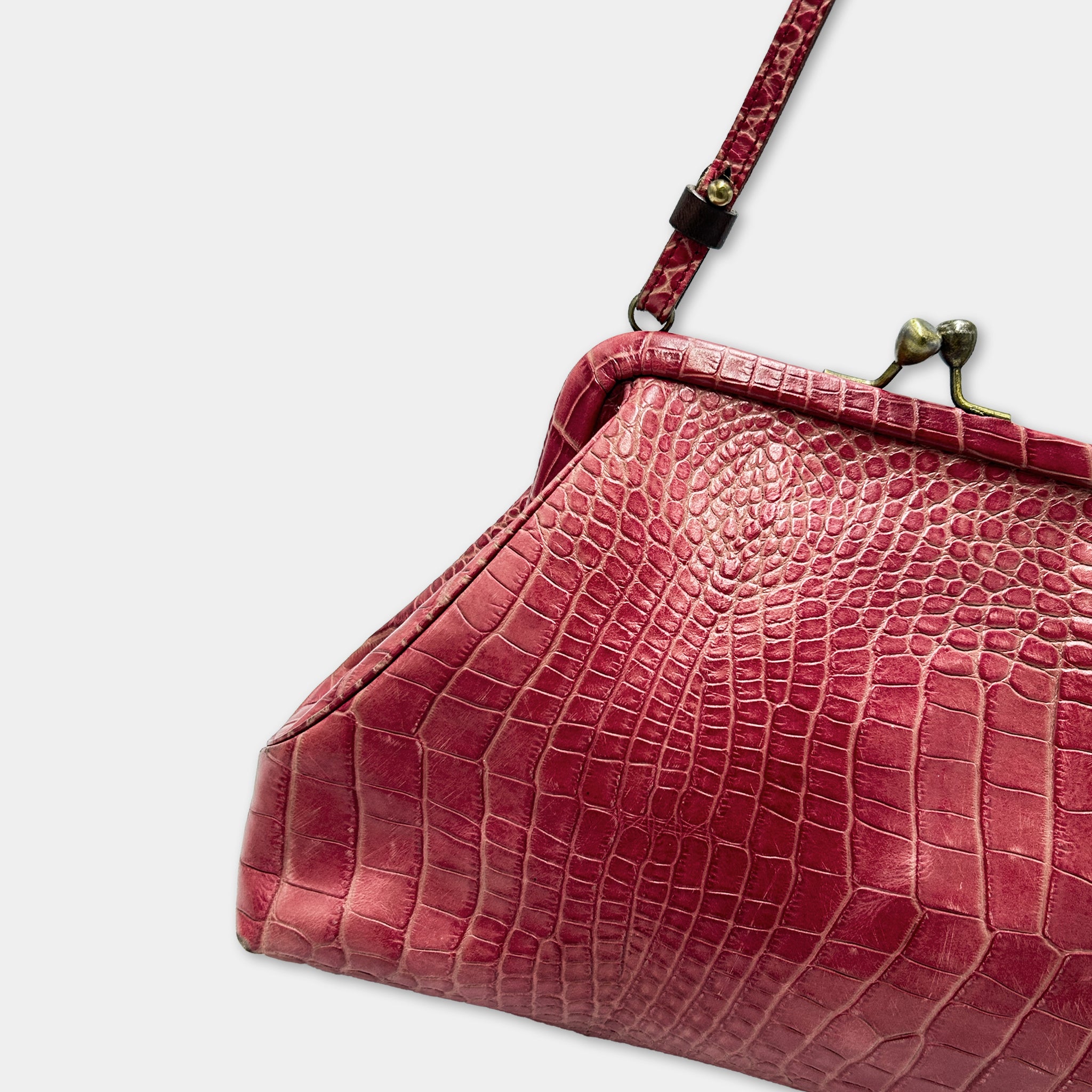 A close-up view of a red, crocodile-skin-like handbag with a metal clasp and strap.