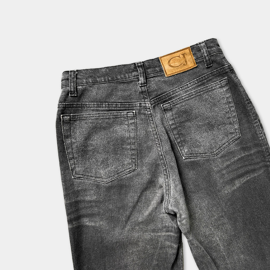 A pair of black jeans with a tan leather patch on the back pocket.