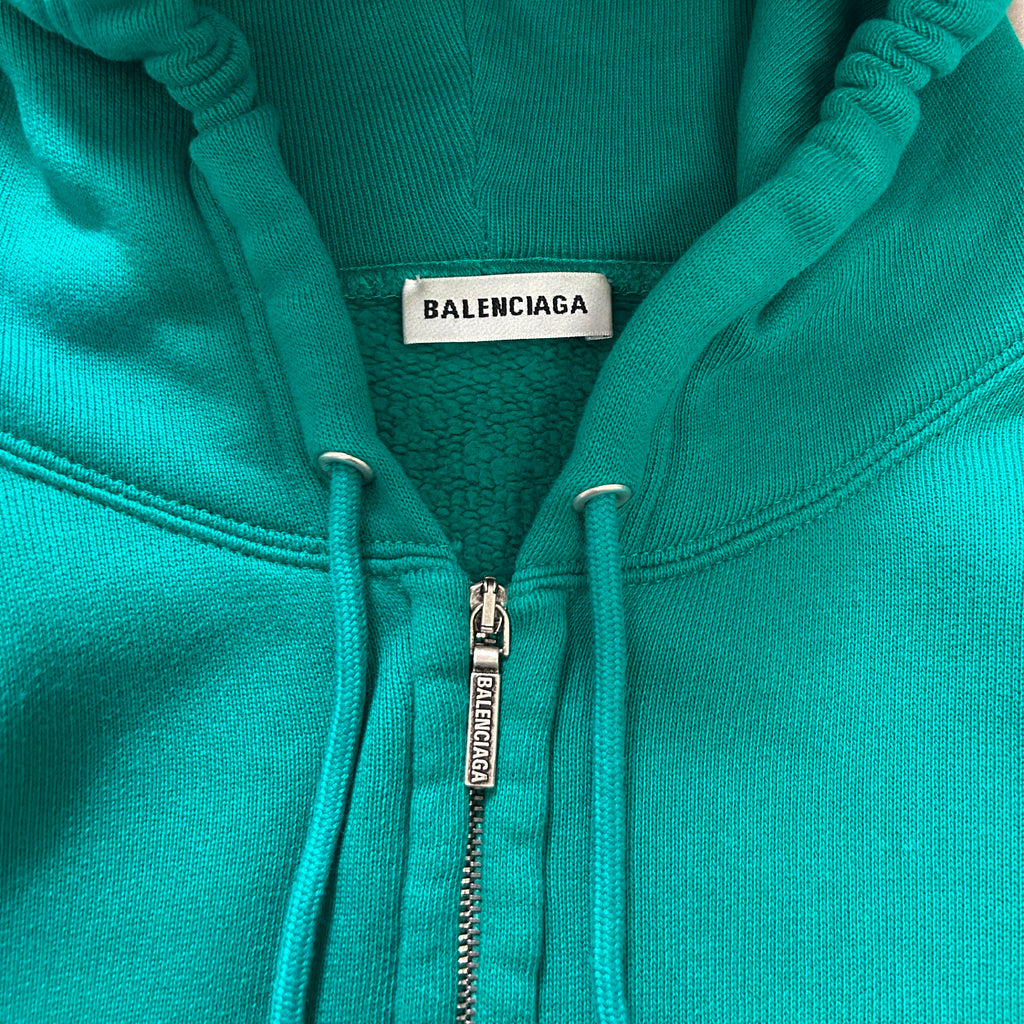A turquoise zip-up hoodie with a Balenciaga label on the front.