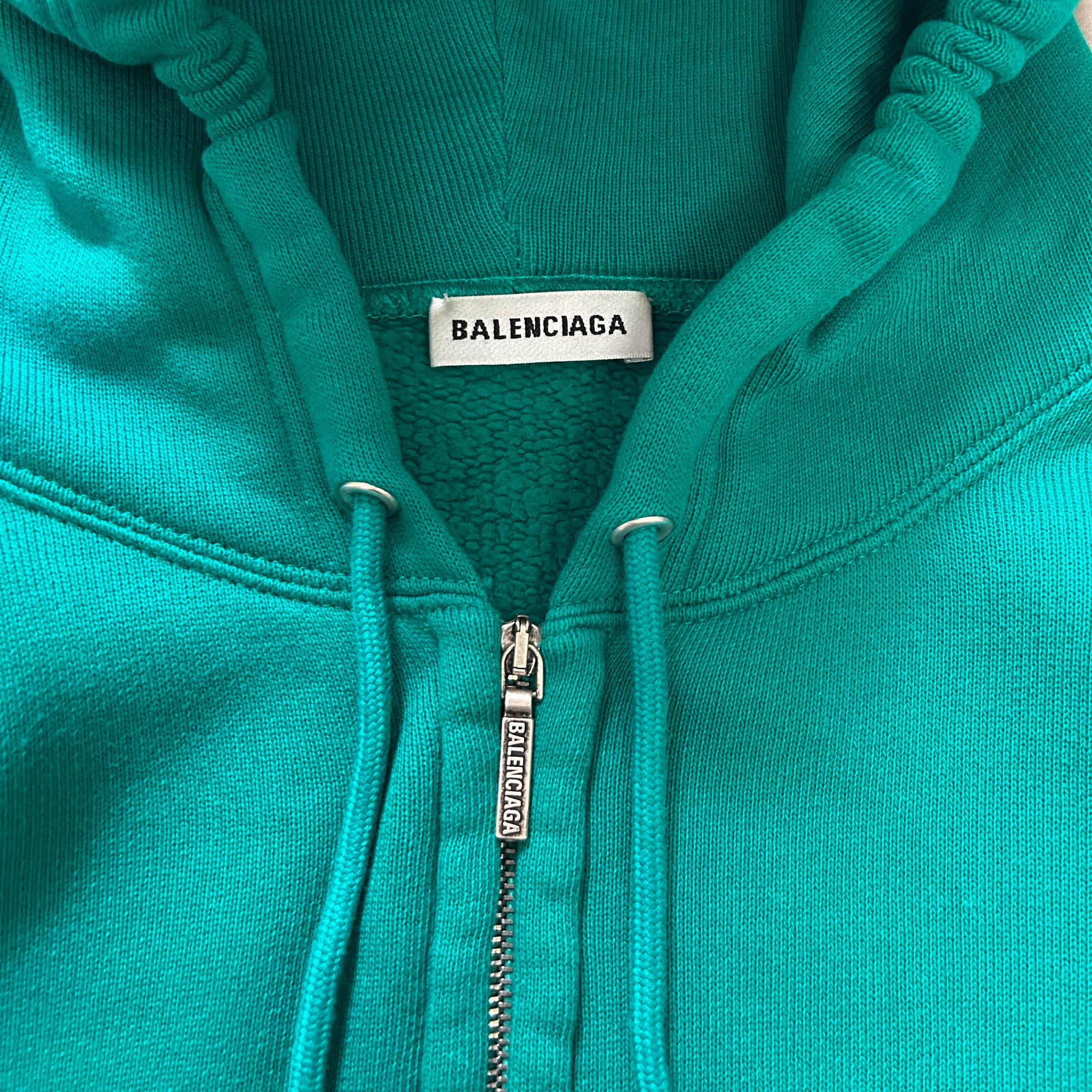 A turquoise zip-up hoodie with a Balenciaga label on the front.